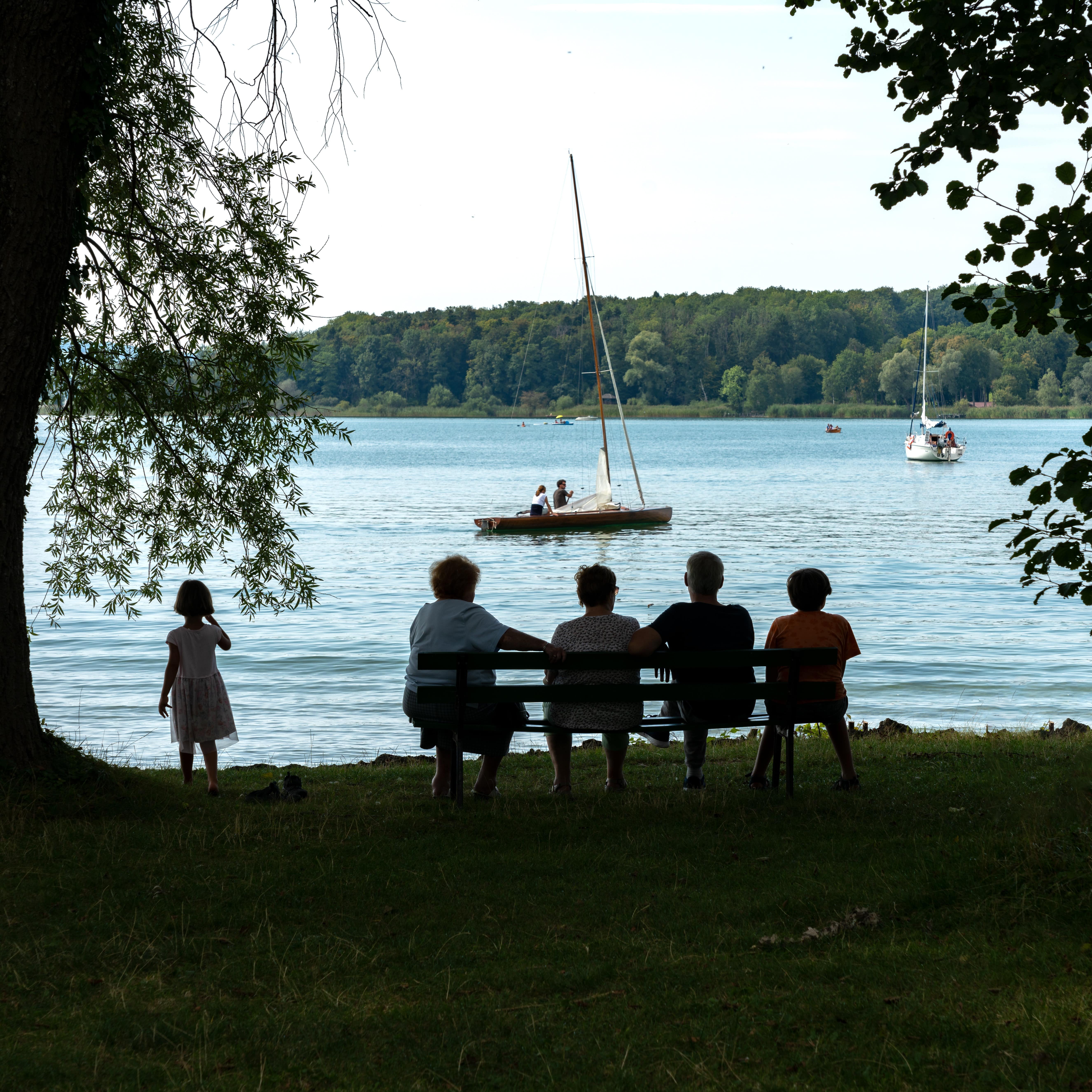 Rückenansicht: Familie mit Kindern auf einer Bank am Chiemsee.