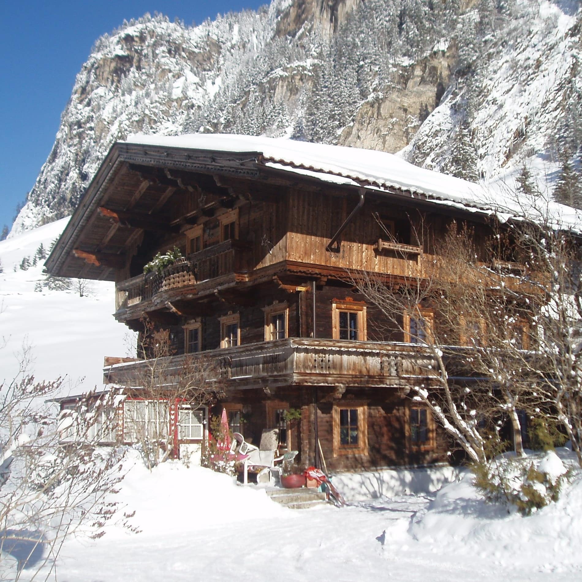 Traditionelles Tiroler Holzhaus mit umlaufendem Balkon in Schneelandschaft 