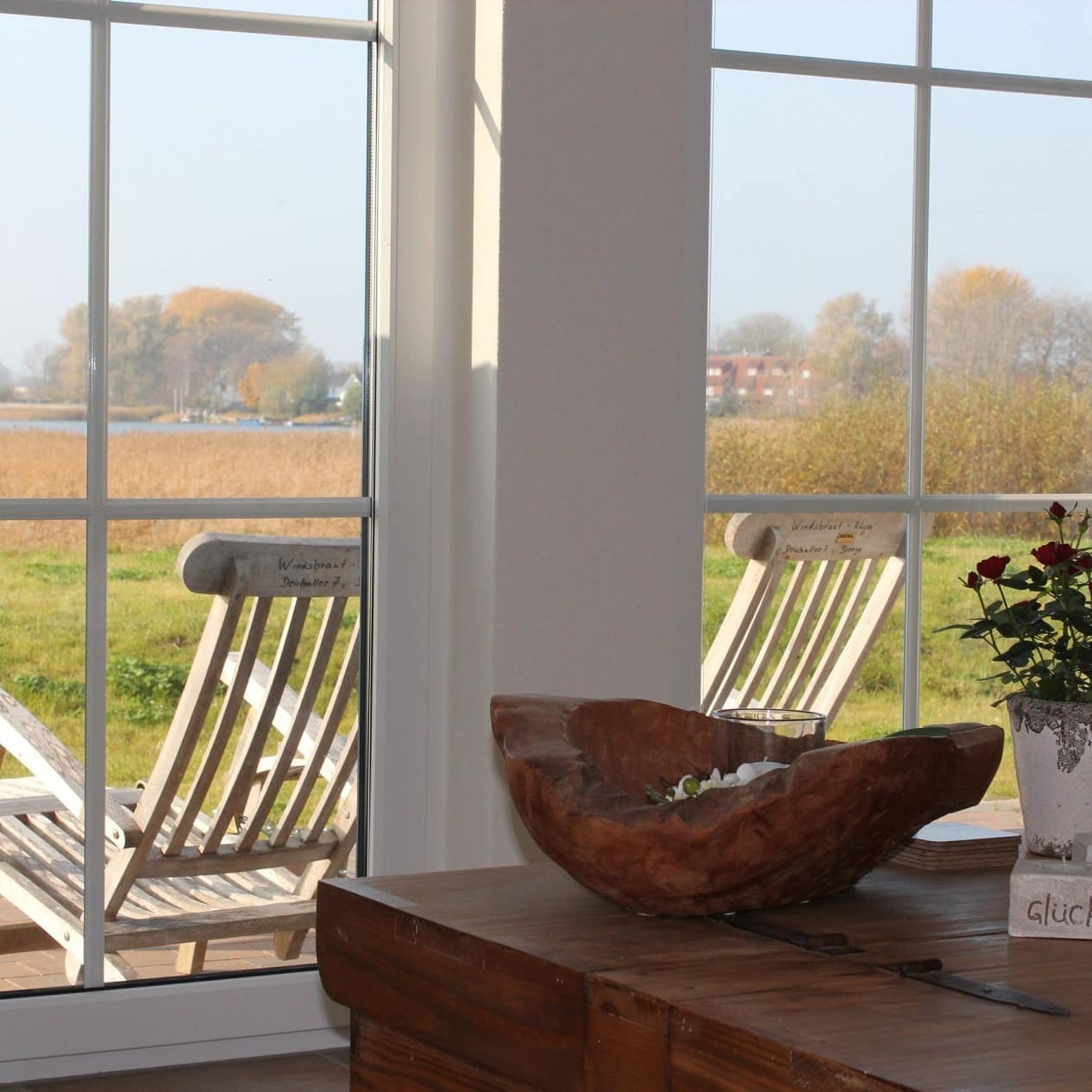 Blick aus dem Wohnzimmer einer Ferienwohnung auf Rügen auf den Garten mit Liegestühlen und das Wasser