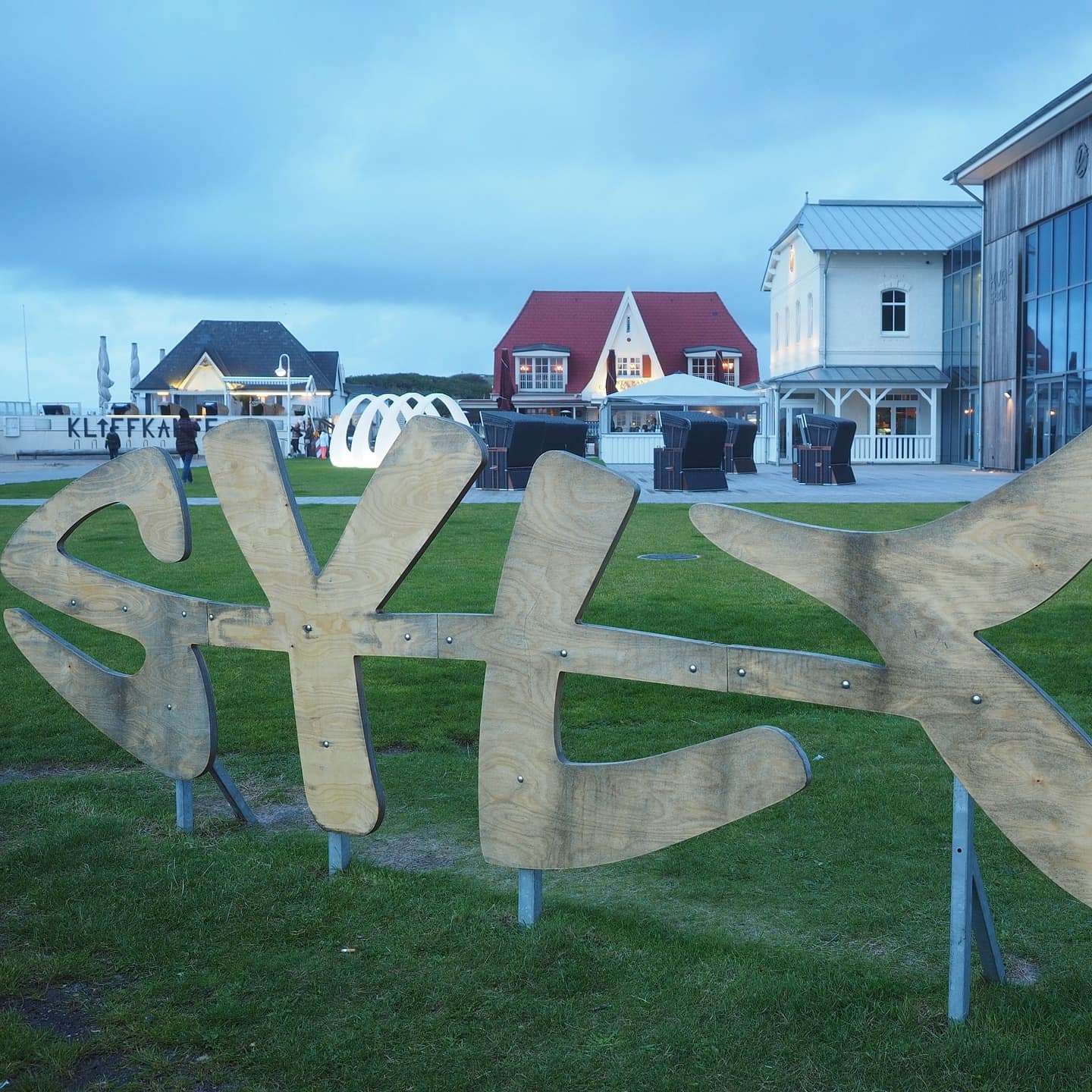 Ein Sylt-Schriftzug in Fischform und Häuser im Hintergrund in Wenningstedt 