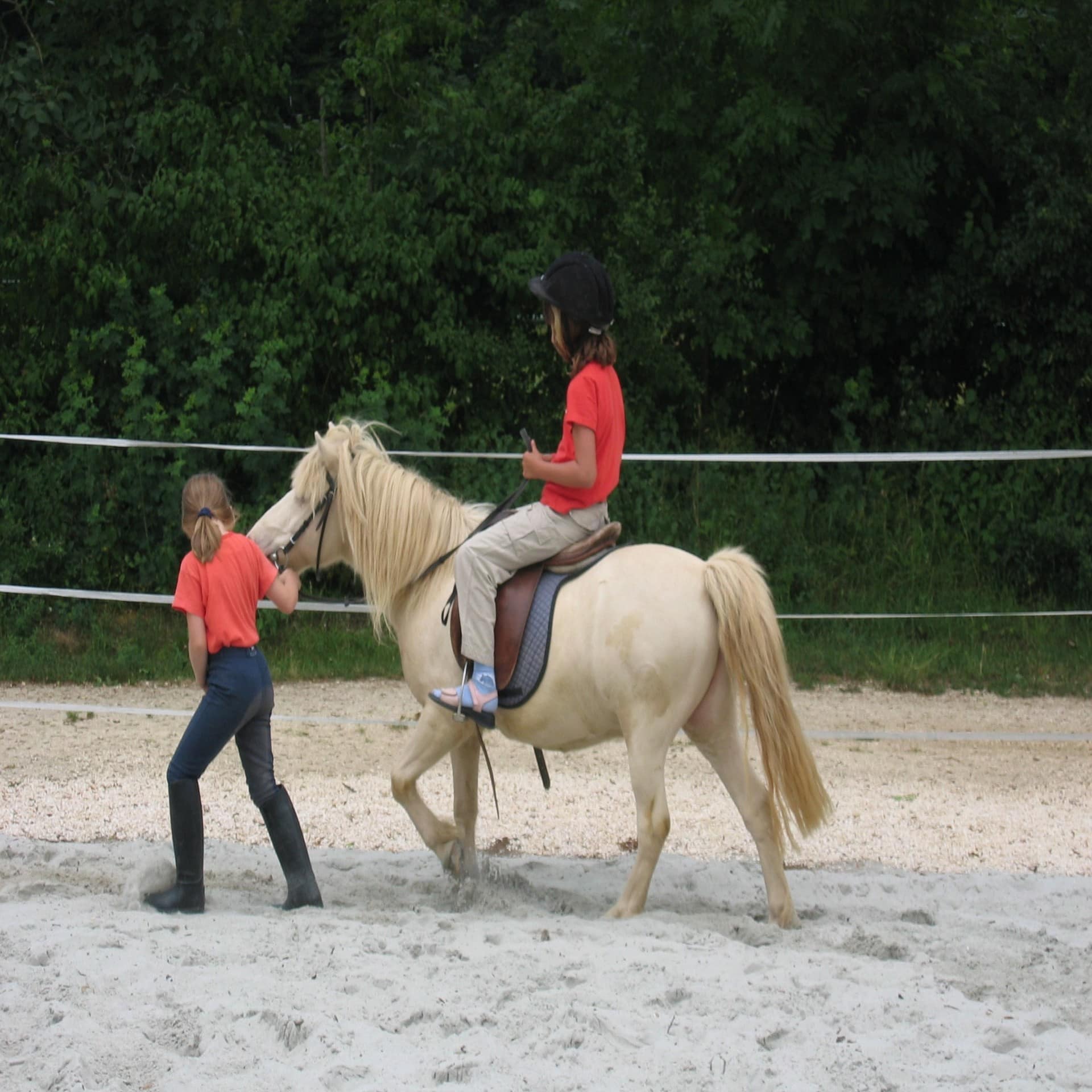 Kind auf einem hellen Pony das von einem Mädchen geführt wird.