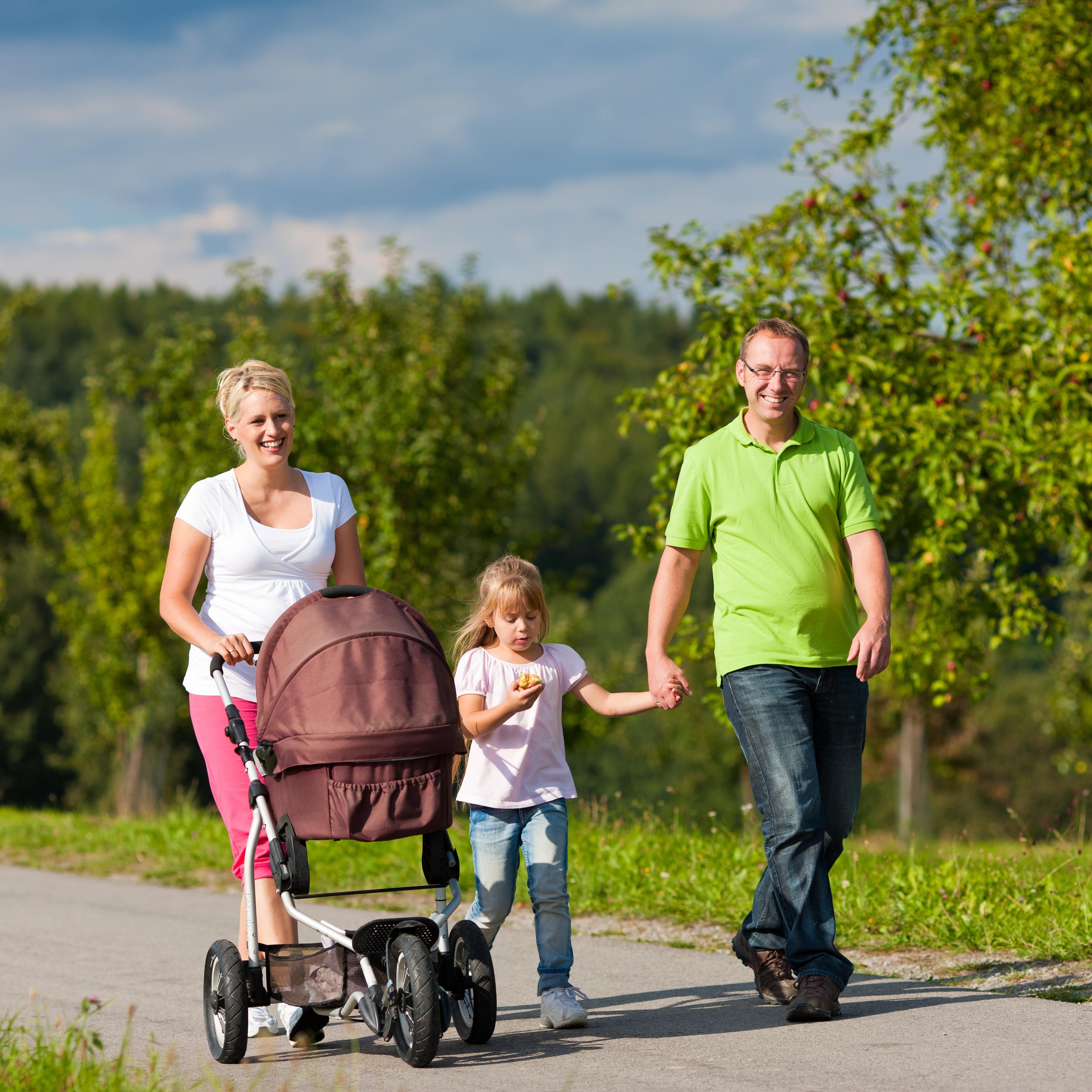 Familie mit Tochter geht spazieren, die Mutter schiebt einen Kinderwagen.