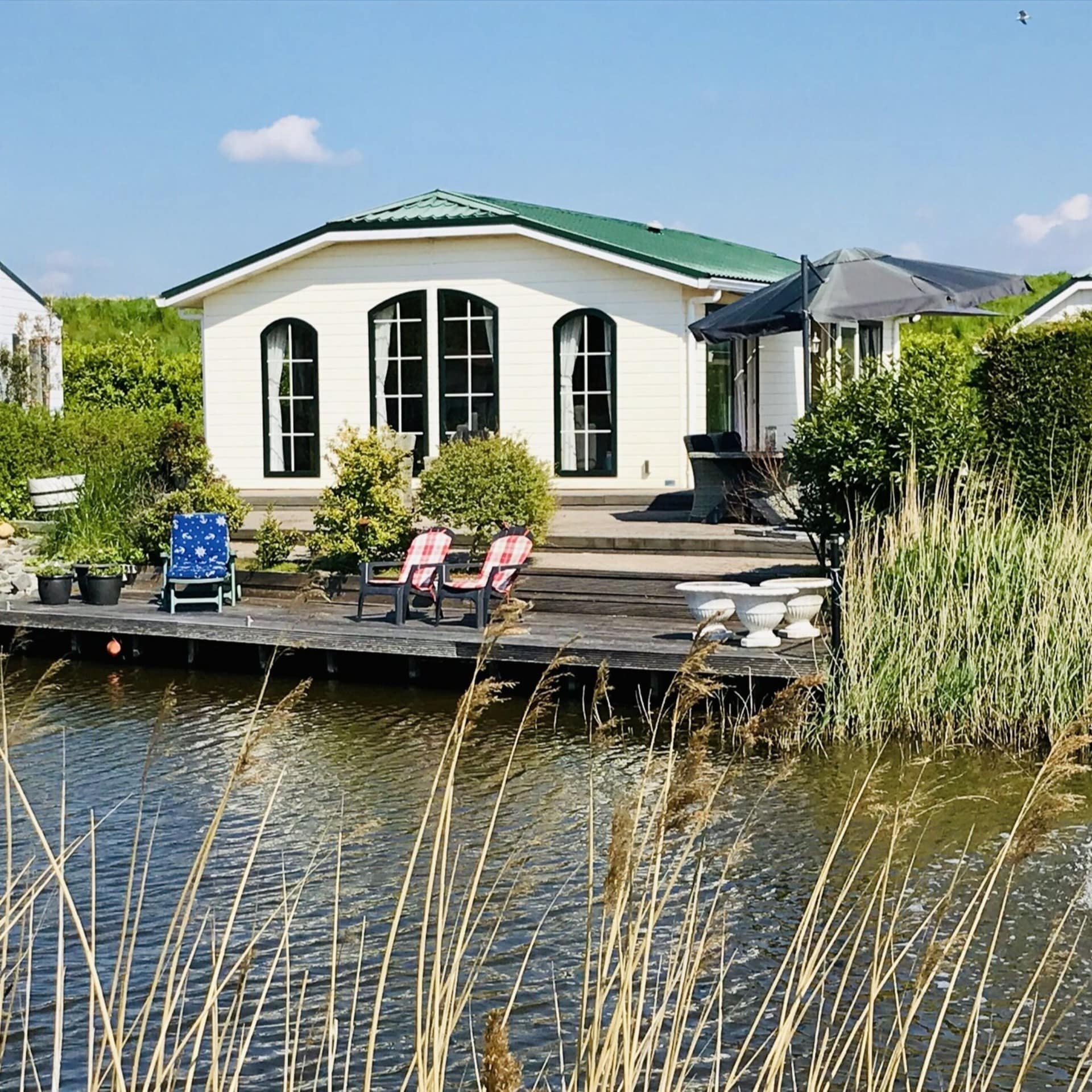 Blick über Wasser auf einen Bungalow mit Holzveranda direkt am Wasser.