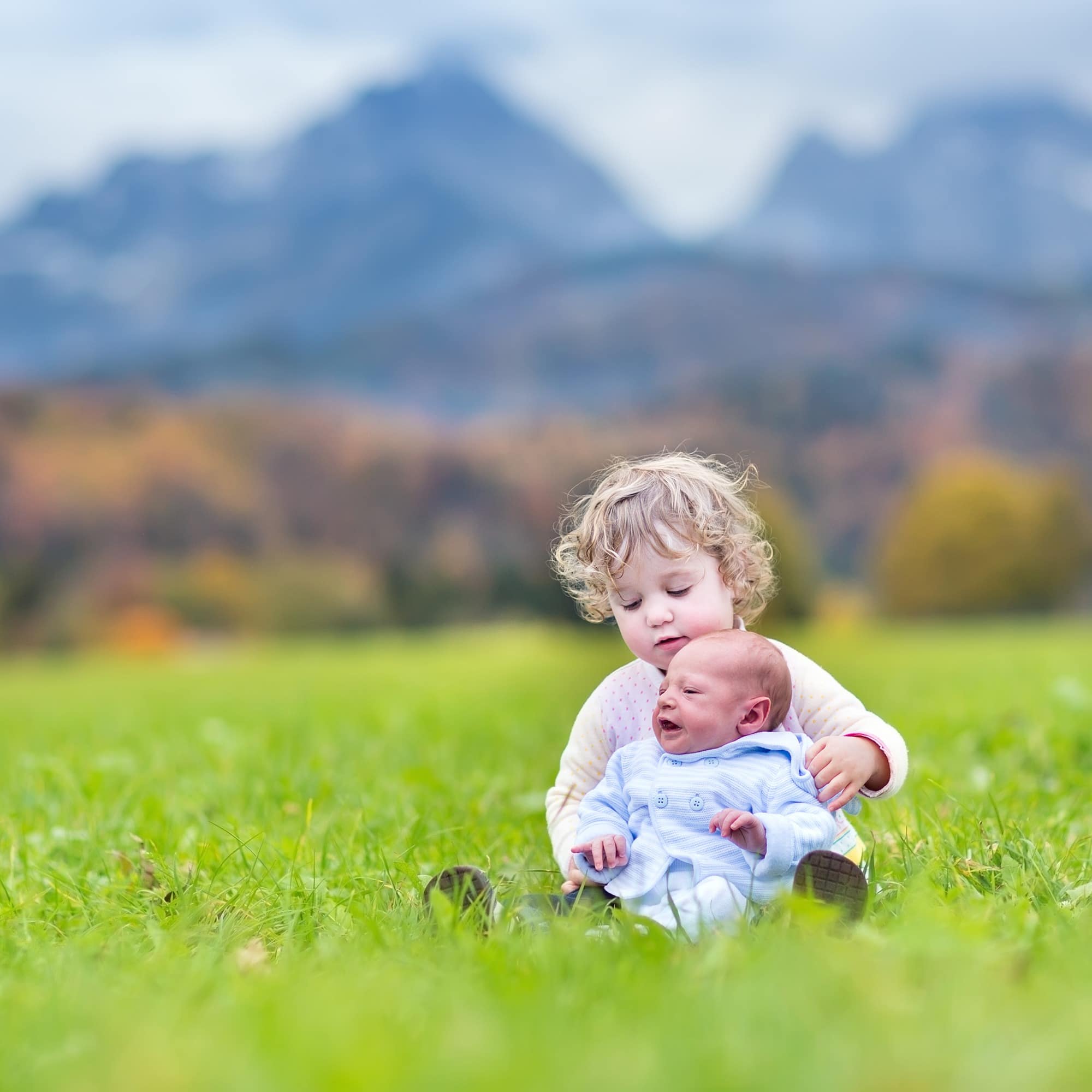 Kleinkind und Baby auf einer Wiese, im Hintergrund die Berge.