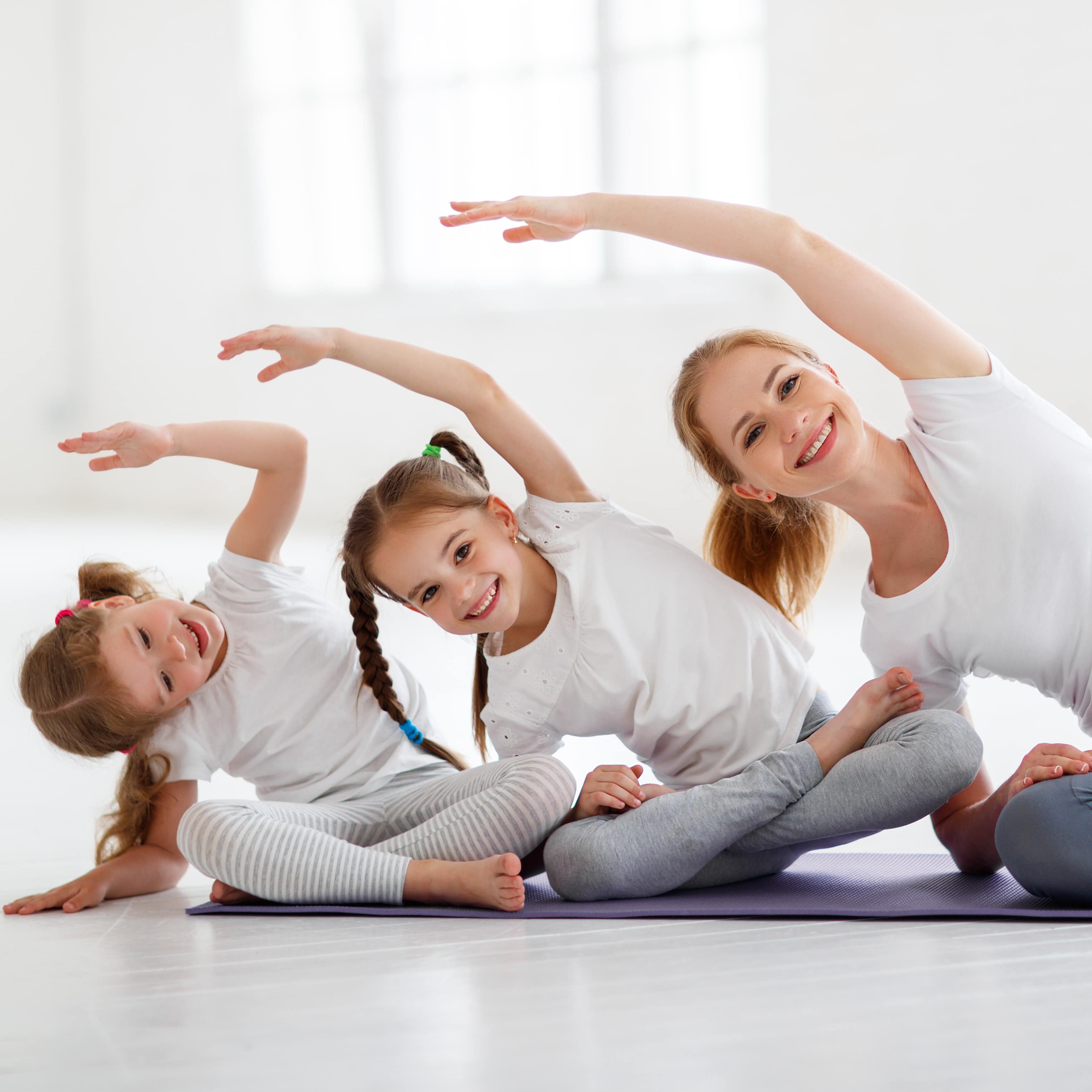 Mutter und 2 Mädchen machen nebeneinander Yoga.