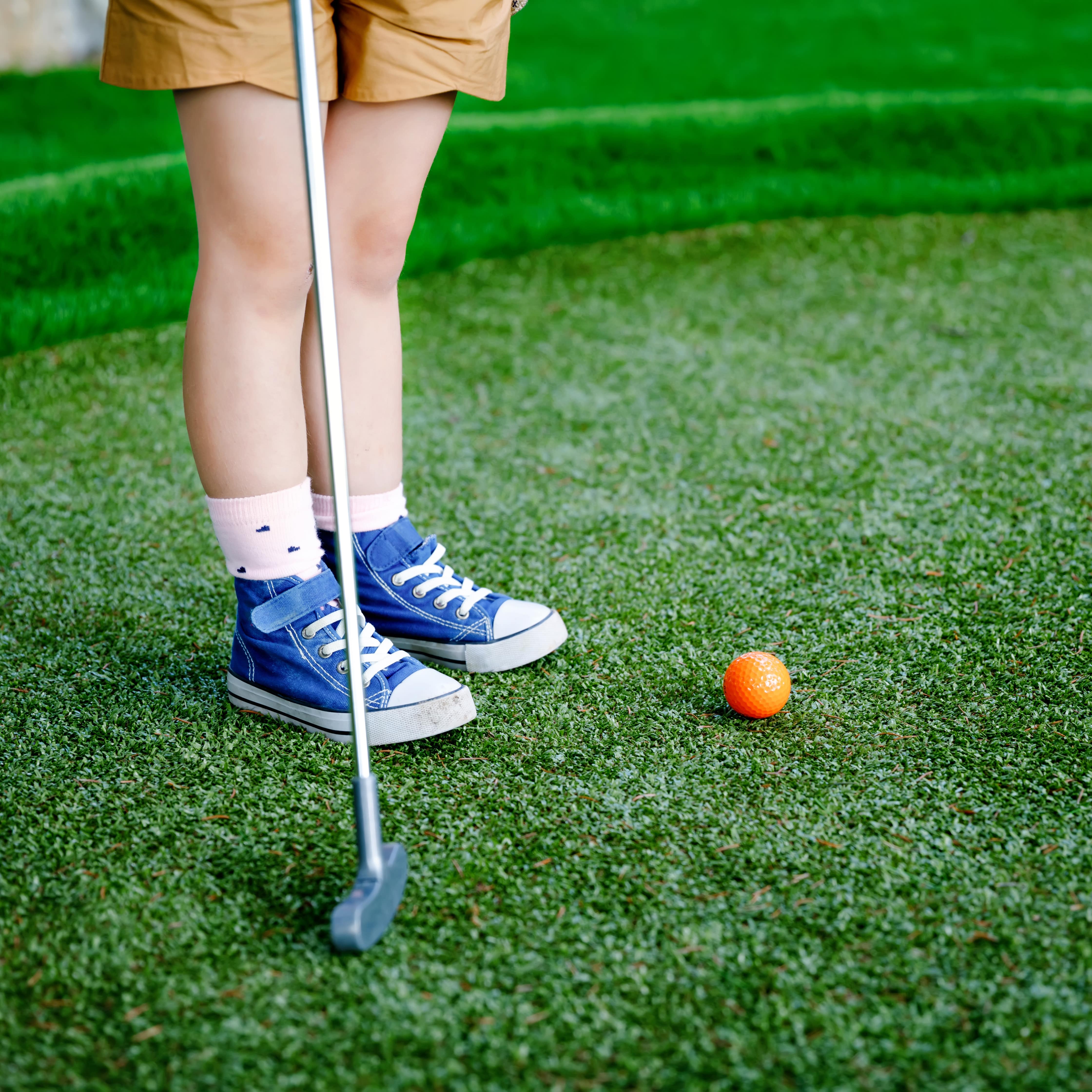 Nahaufnahme: Die Unterbeine eines Kinds das Minigolf spielt.