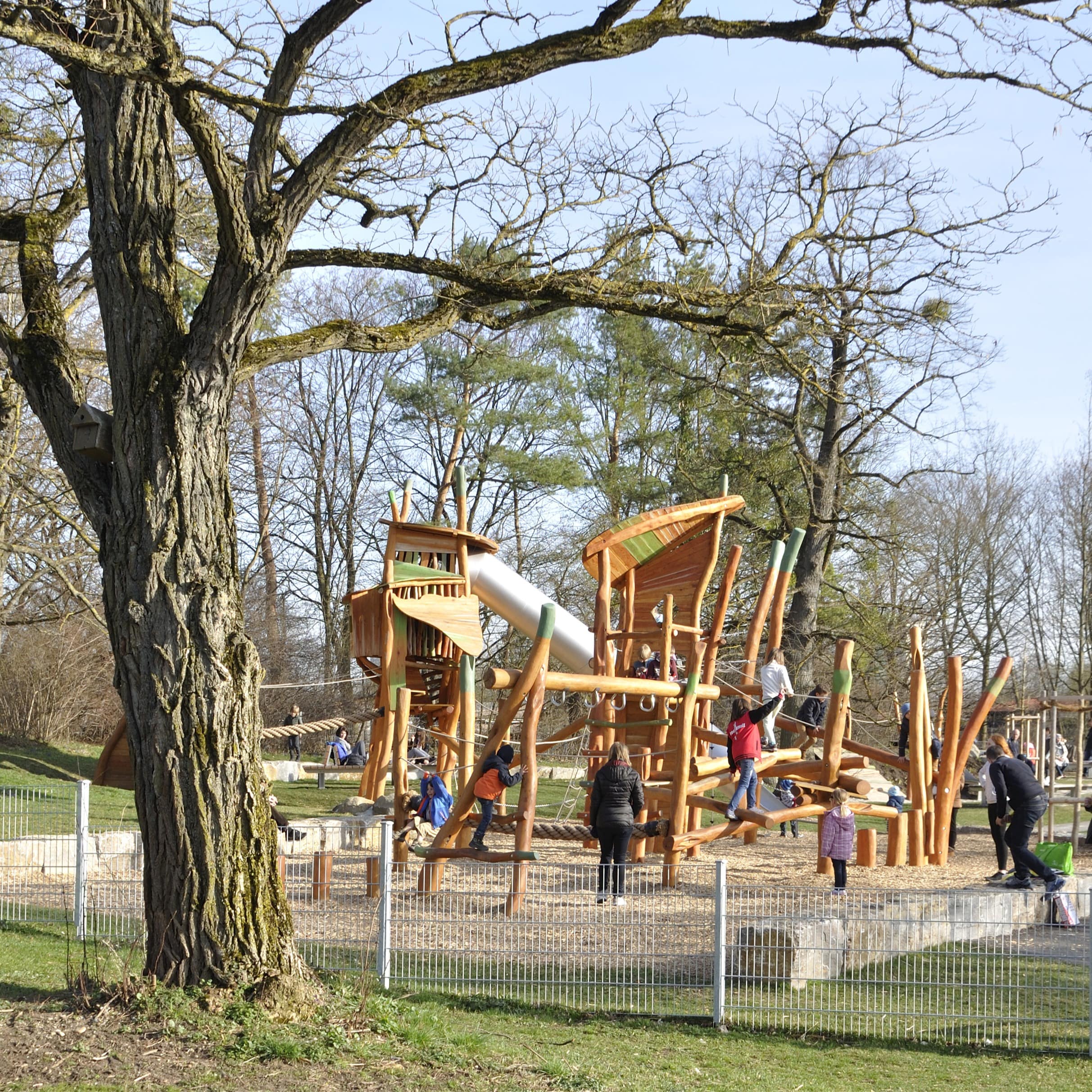 Blick auf einen Spielplatz mit großem Holzklettergerüst in einem Park im München. 