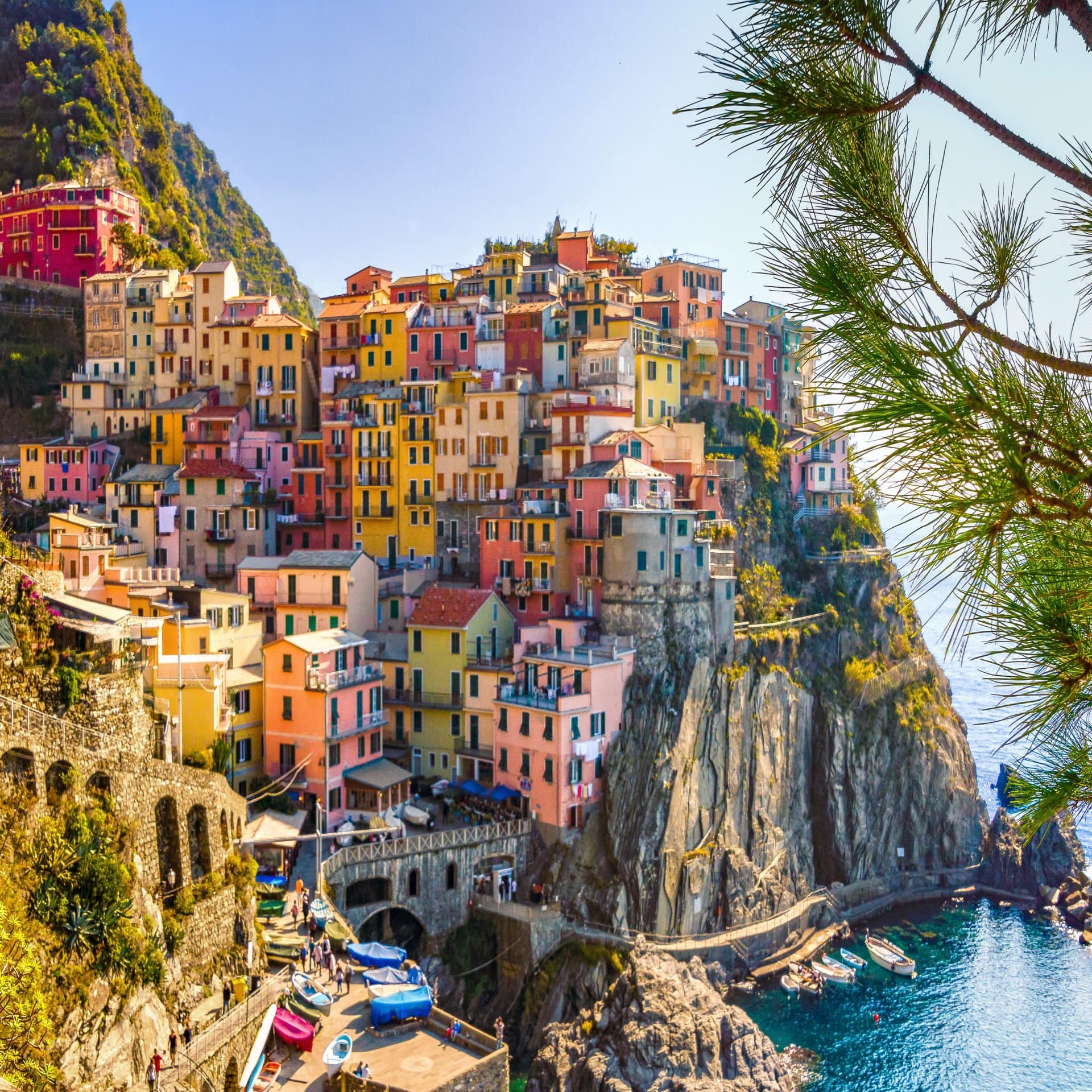 Cinque Terre: Bunte Häuser auf den Felsen, daneben das Meer. Die Sonne scheint. 