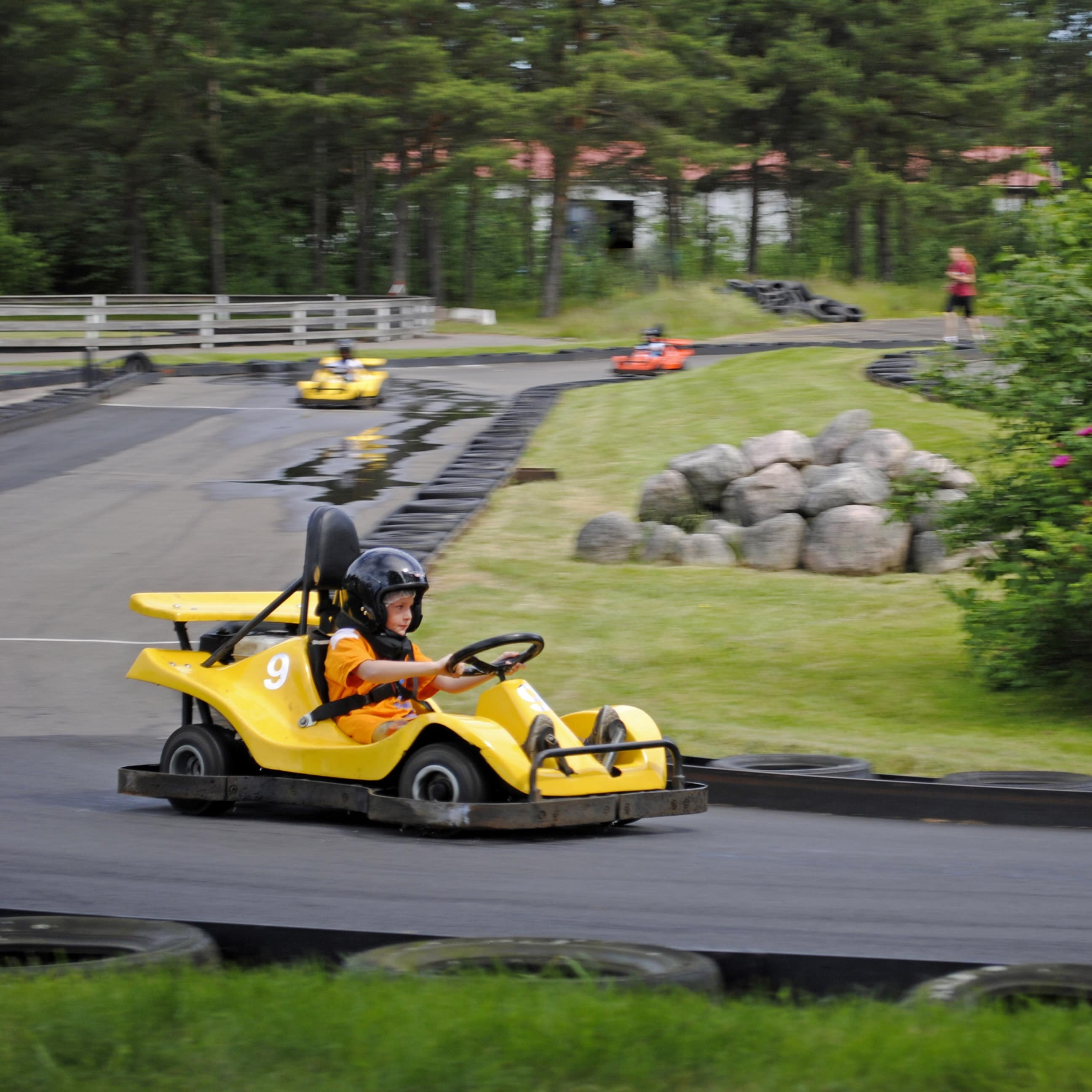 Junge in Sommerkleidung und mit Helm in einem gelben Kart auf einer Kartbahn.