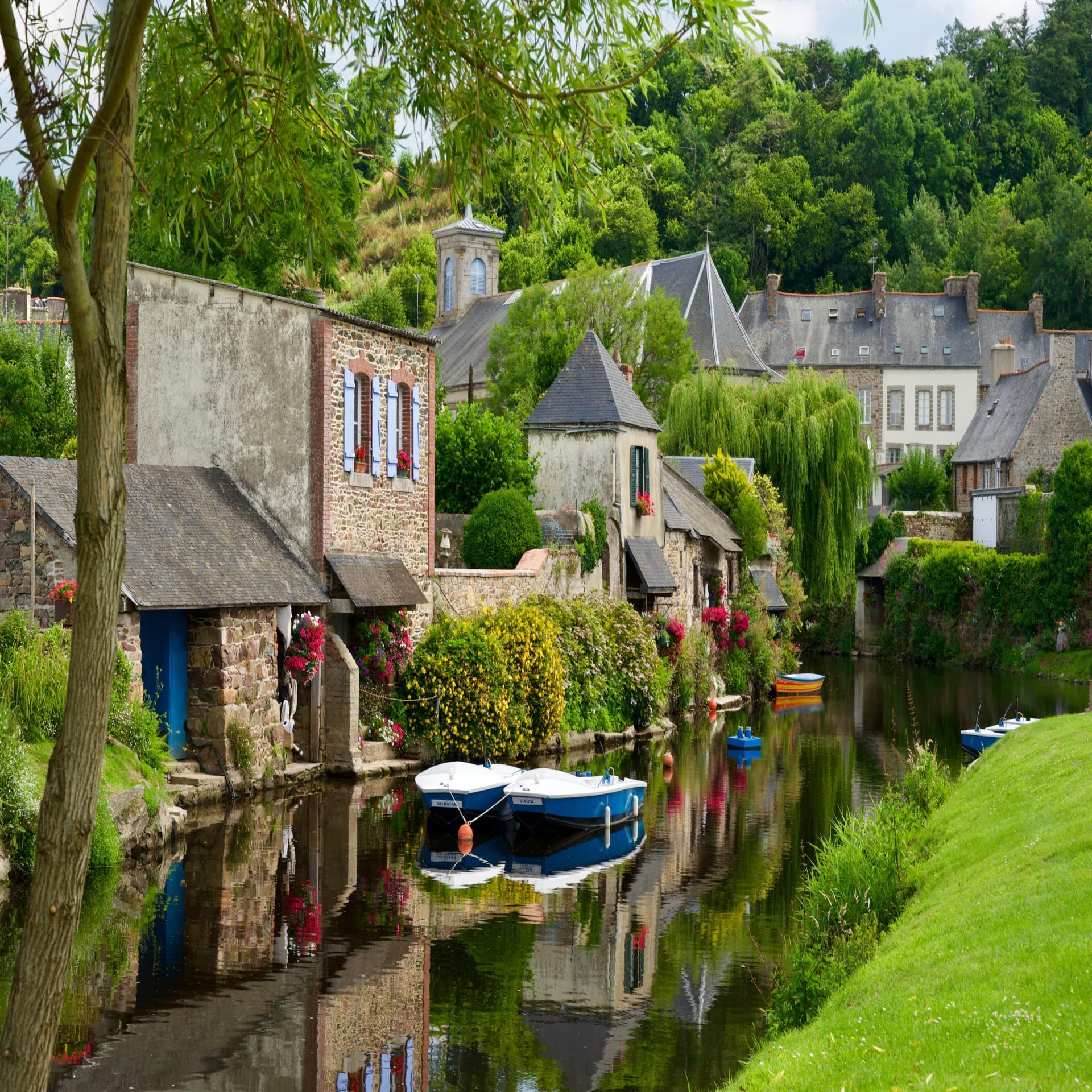 Steinhäuser, blühende Büsche und Bäume direkt an einem Fluss.