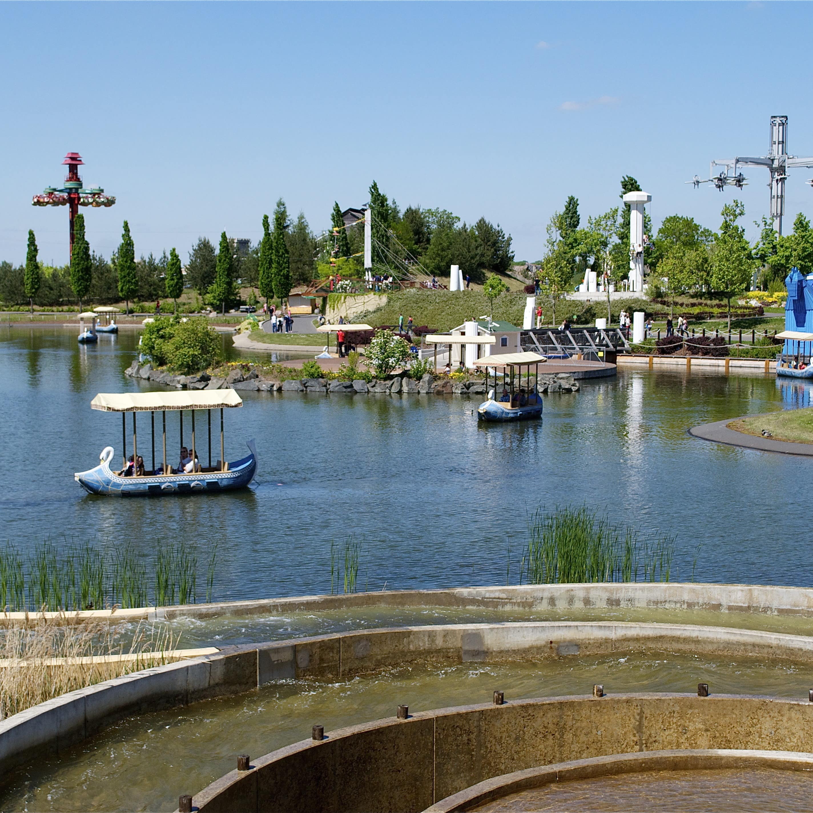 Blick über einen See mit kleinen Booten und Fahrattraktionen im Belantis Vergnügungspark.