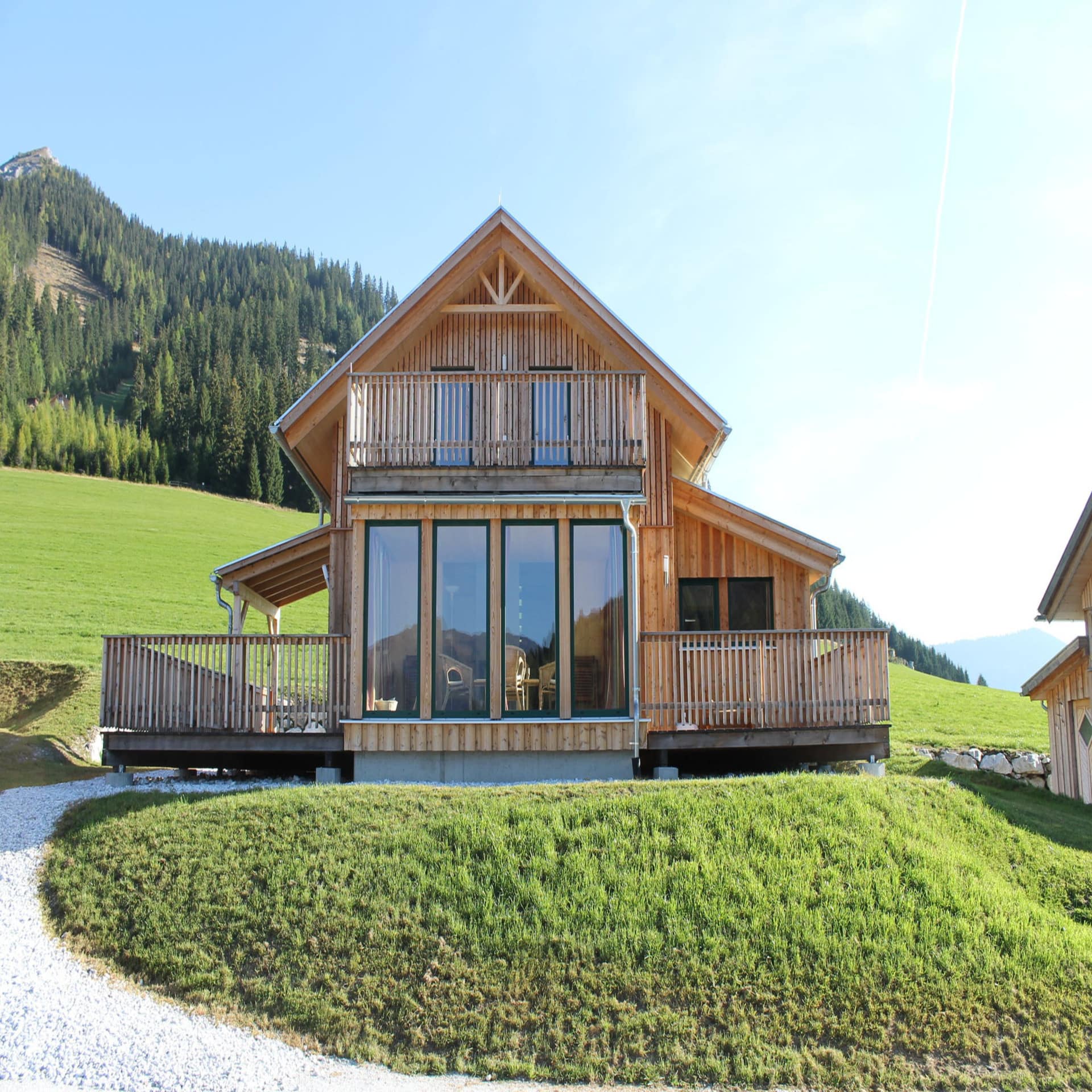 Eine moderne Holzhütte am Hang, im Hintergrund eine grüne Wiese und Bäume.