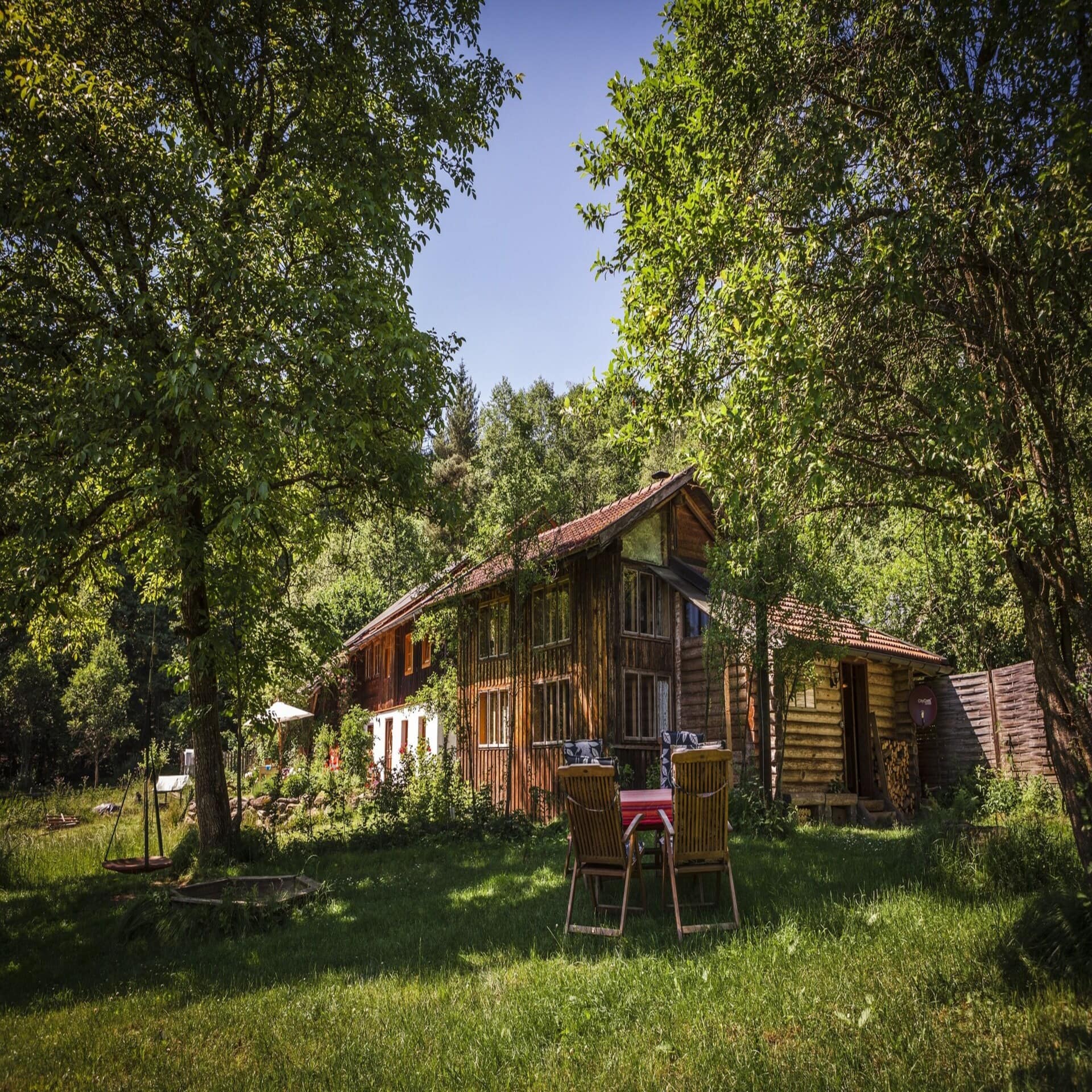 Ein Holzhaus mit großem Garten in dem ein runder Tisch und Stühle stehen.