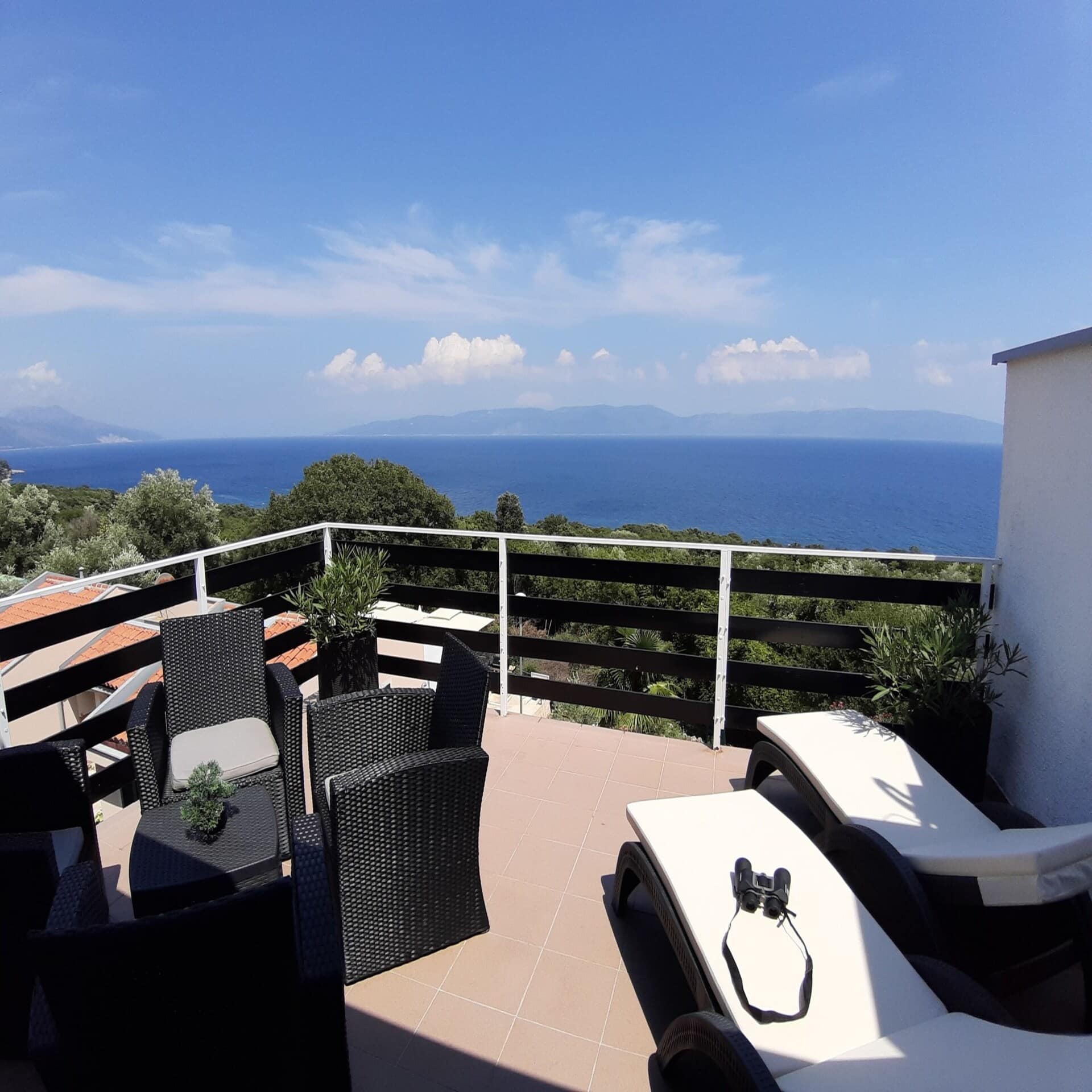Großer sonniger Balkon mit Liegestühlen und Sitzgelegenheiten sowie Blick auf das Meer.