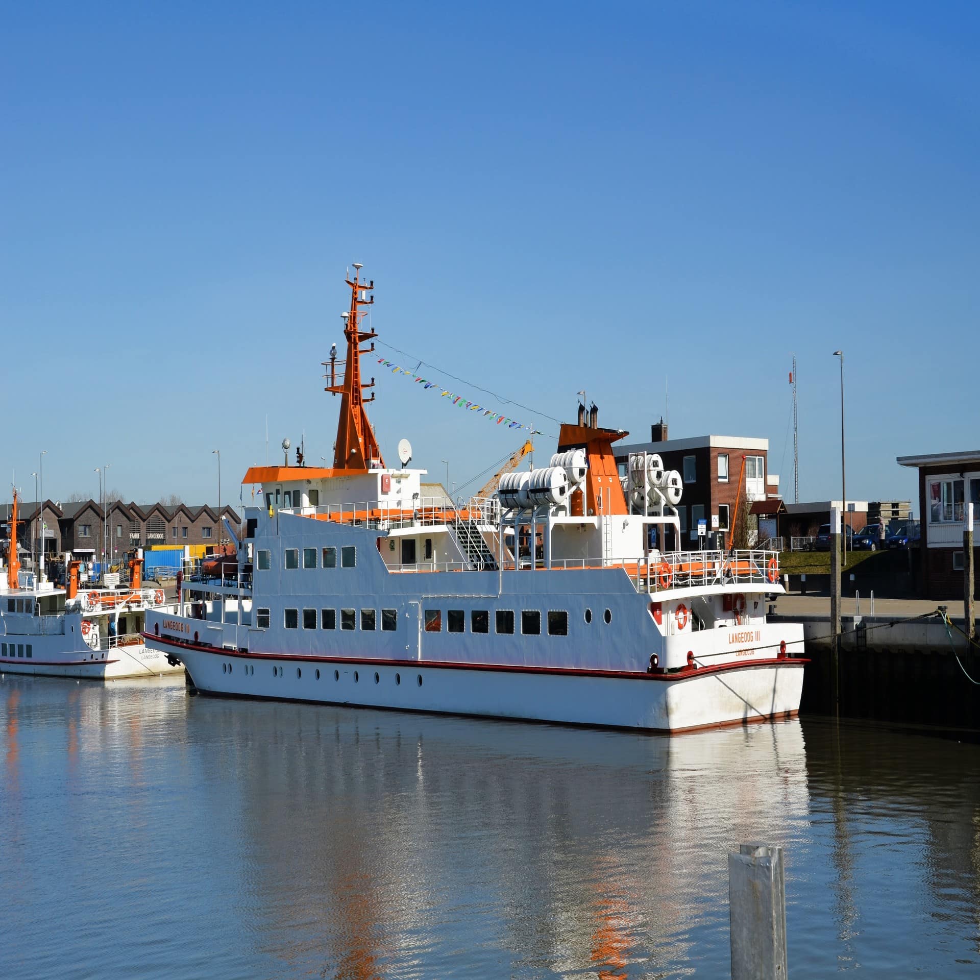 Ein weißes Schiff im Hafen von Bensersiel, dahinter sind Gebäude zu sehen. 
