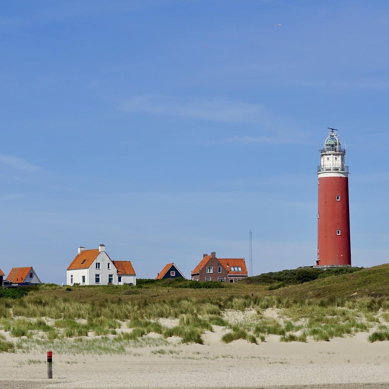 Blick vom Strand auf mehrere Häuser und einen Leuchtturm auf Texel