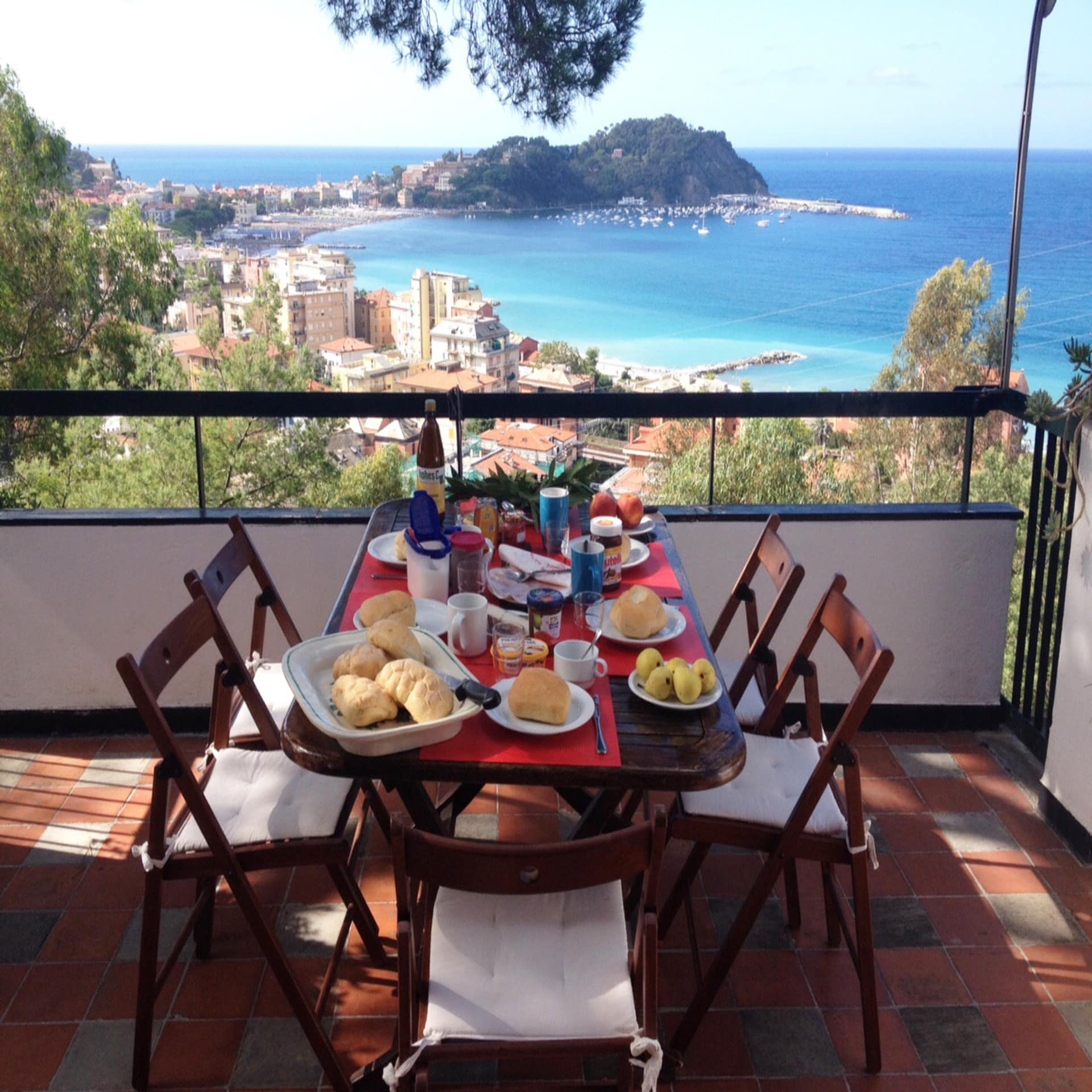 Terrasse mit gedecktem Frühstückstisch für 5 Personen und Blick auf einen Ort und eine Bucht.