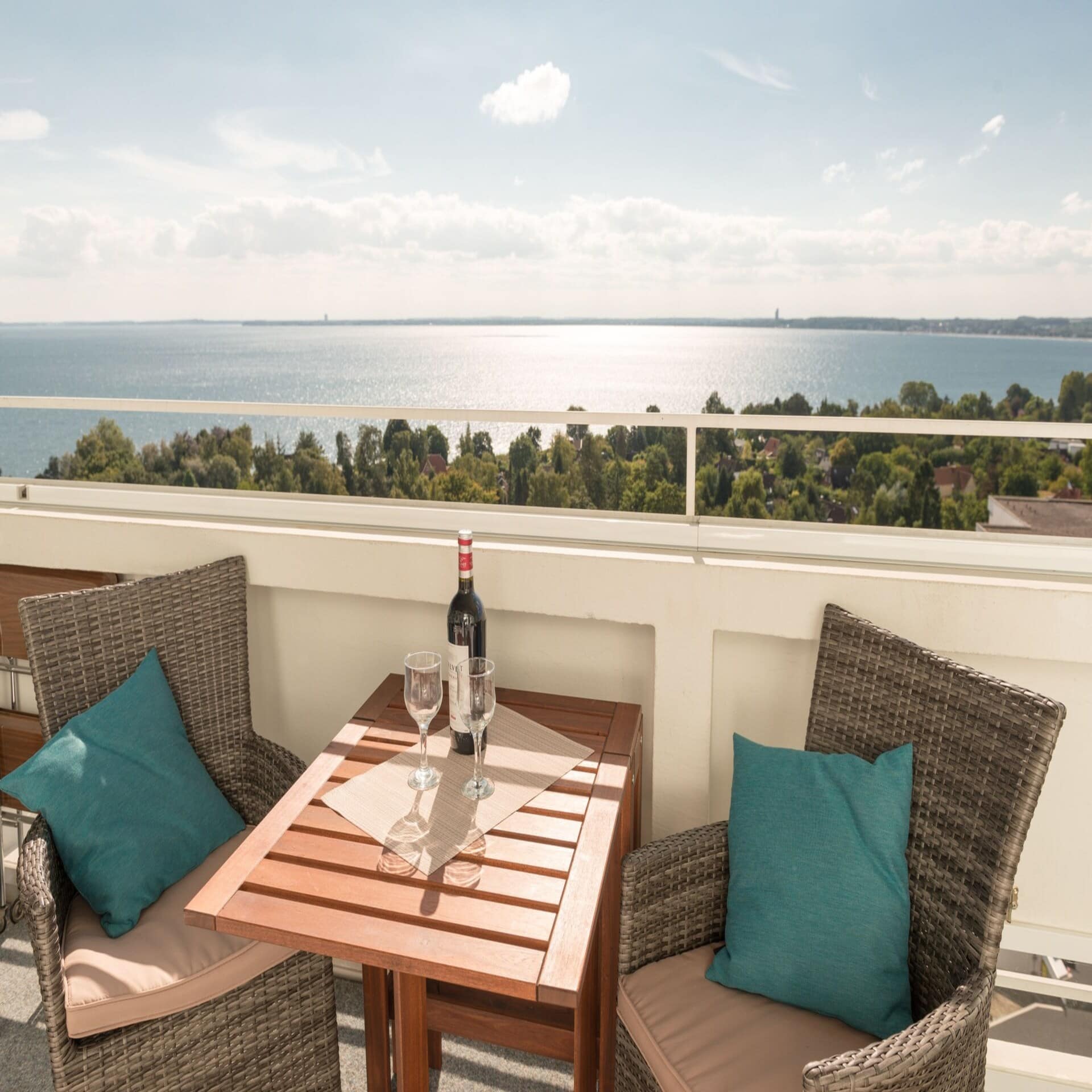Balkon mit Tisch, Stühlen und Wein sowie Blick auf die Ostsee bei Sonnenschein. 