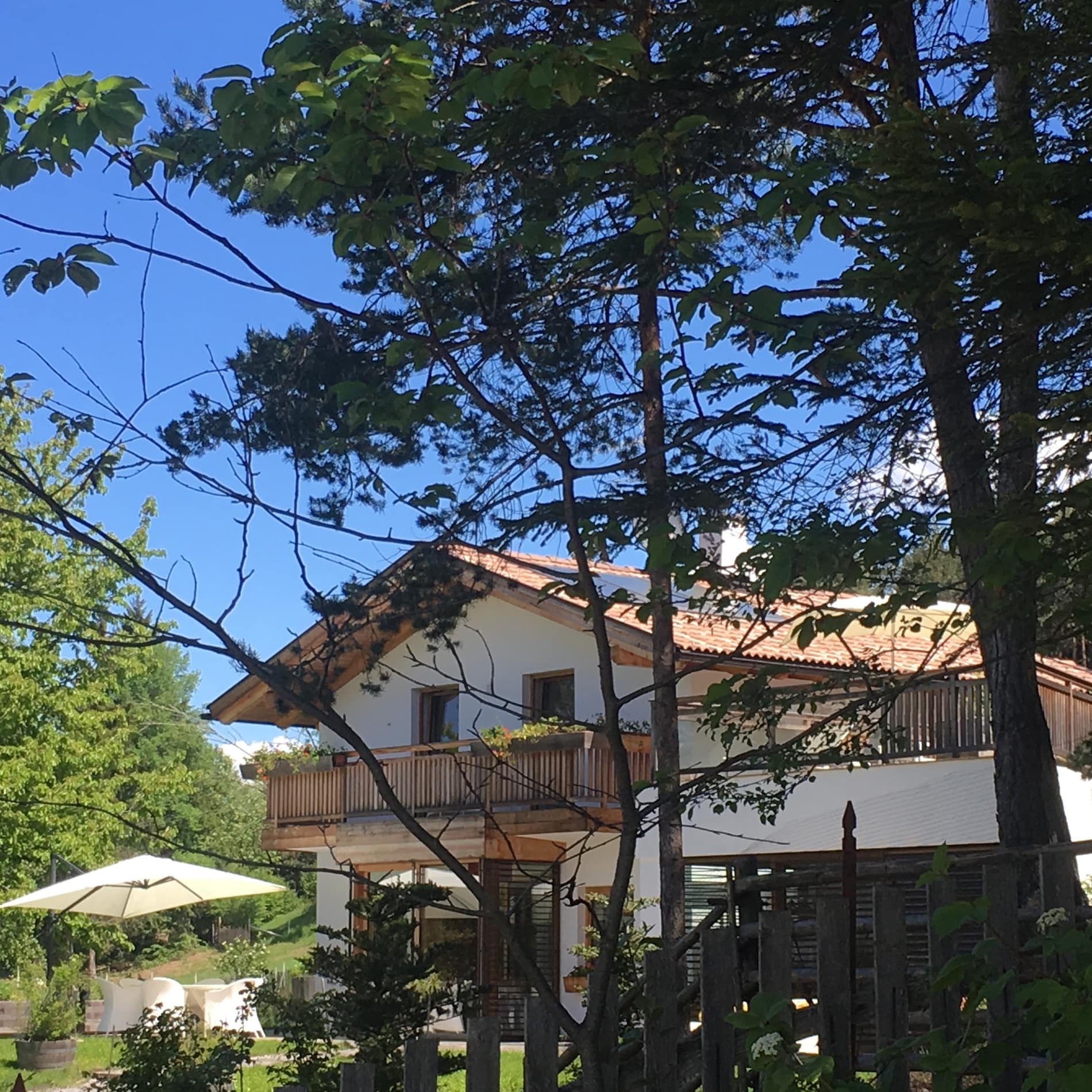 Ferienhaus zwischen Bäumen mit einer Sitzgruppe unter einem Sonnenschirm