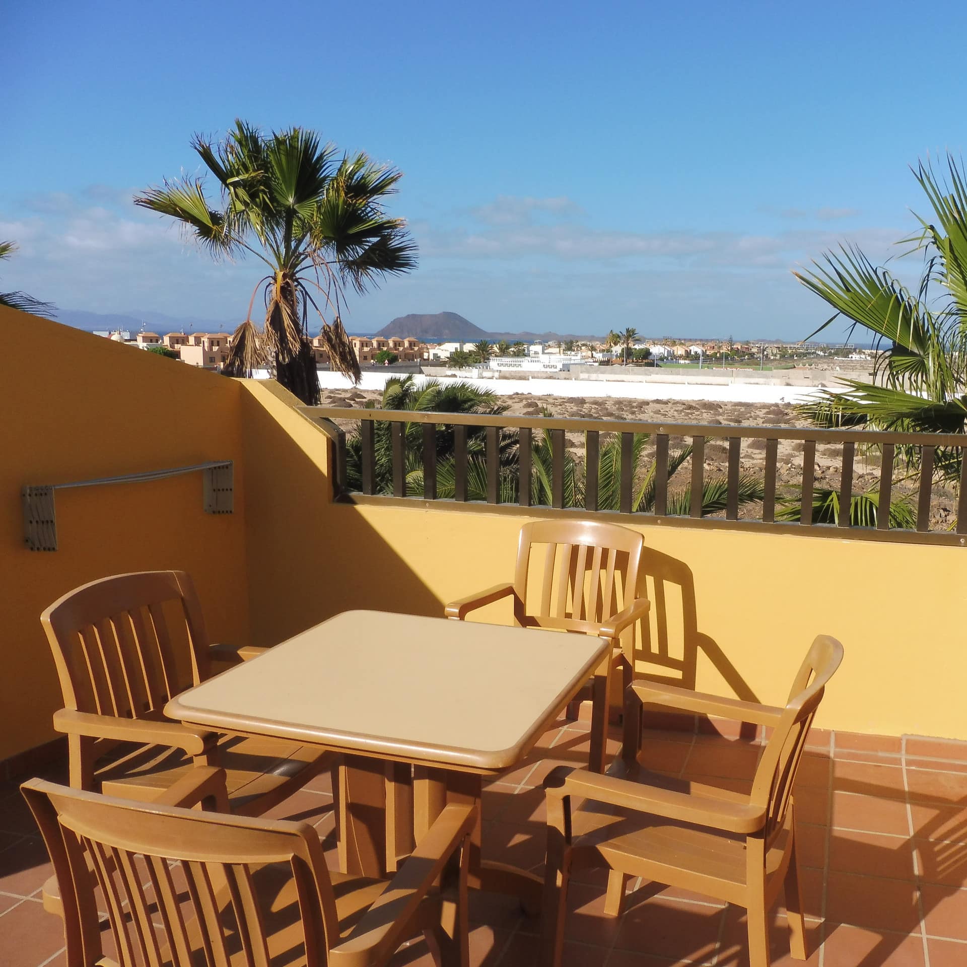 Ferienwohnung auf Fuerteventura mit großem Balkon, darauf Tisch und Stühle, und Weitblick übers Meer und eine Insel