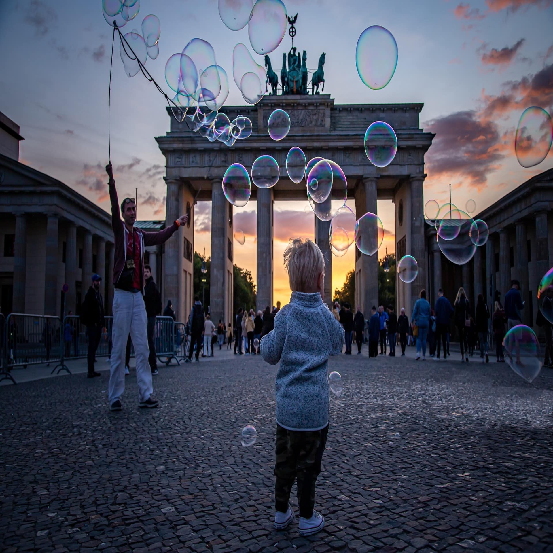 Sonnenuntergang: Ein kleiner Junge umgeben von Seifenblasen vor dem Brandenburger Tor. Rückenansicht. 