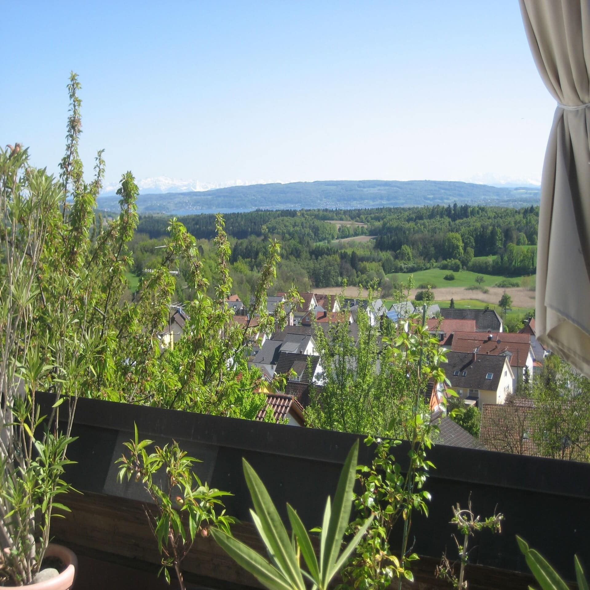 Balkon mit Ausblick auf einen Ort und eine grüne, hügelige Landschaft.