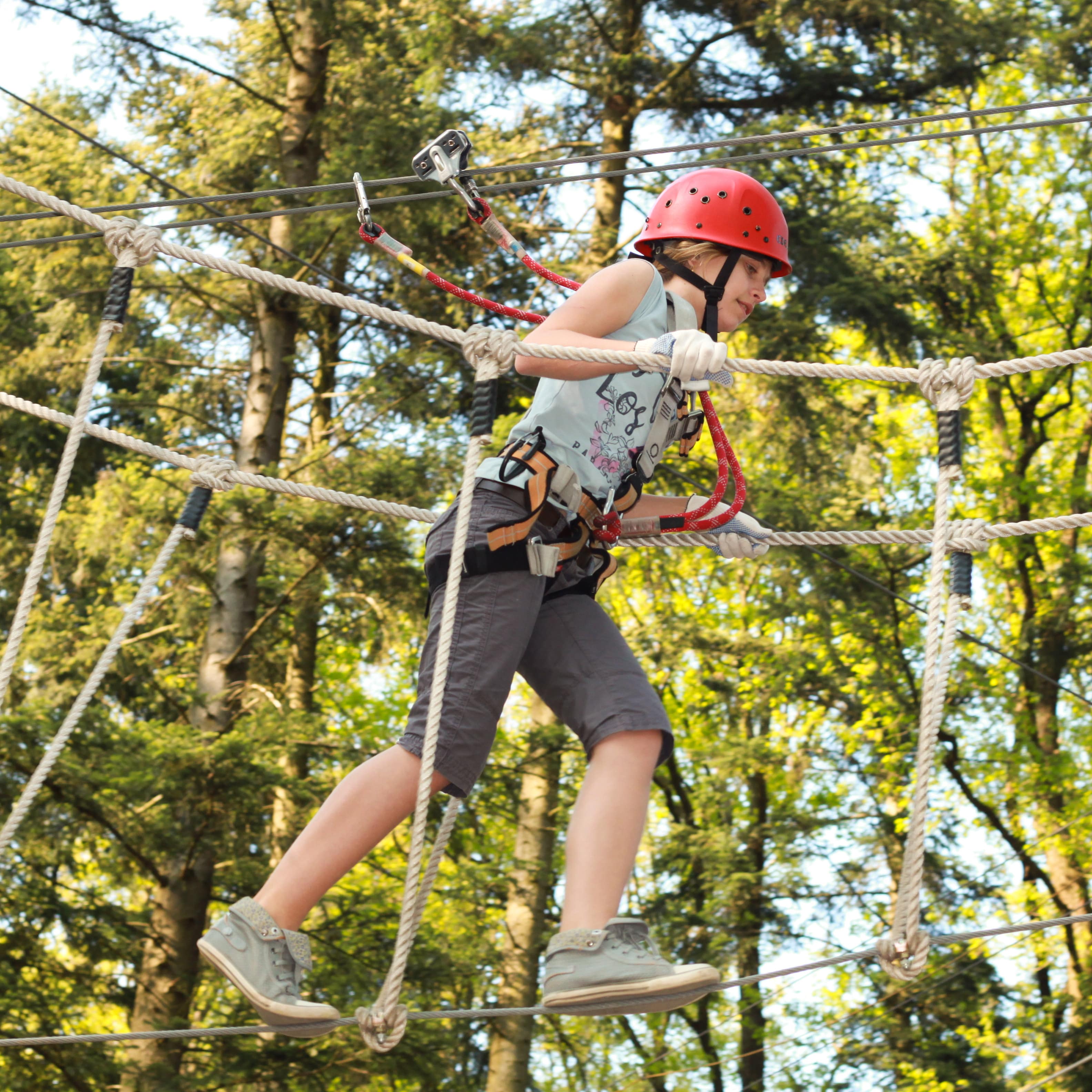 Ein Mädchen mit Kletterausrüstung in einem Hochseilgarten. 