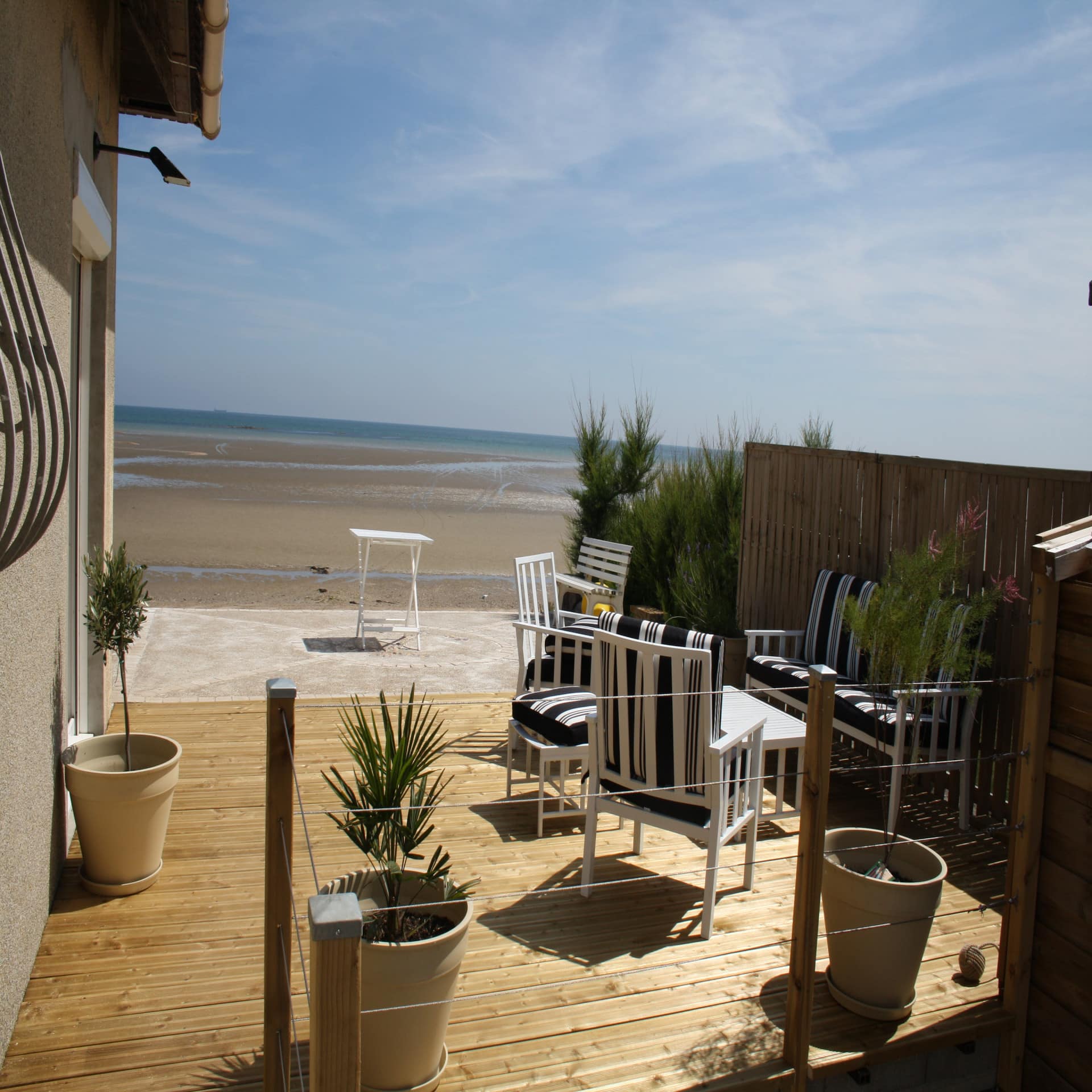 Haus mit Holzveranda und Sitzgelegenheiten direkt am Strand der Normandie. Die Sonne scheint. 