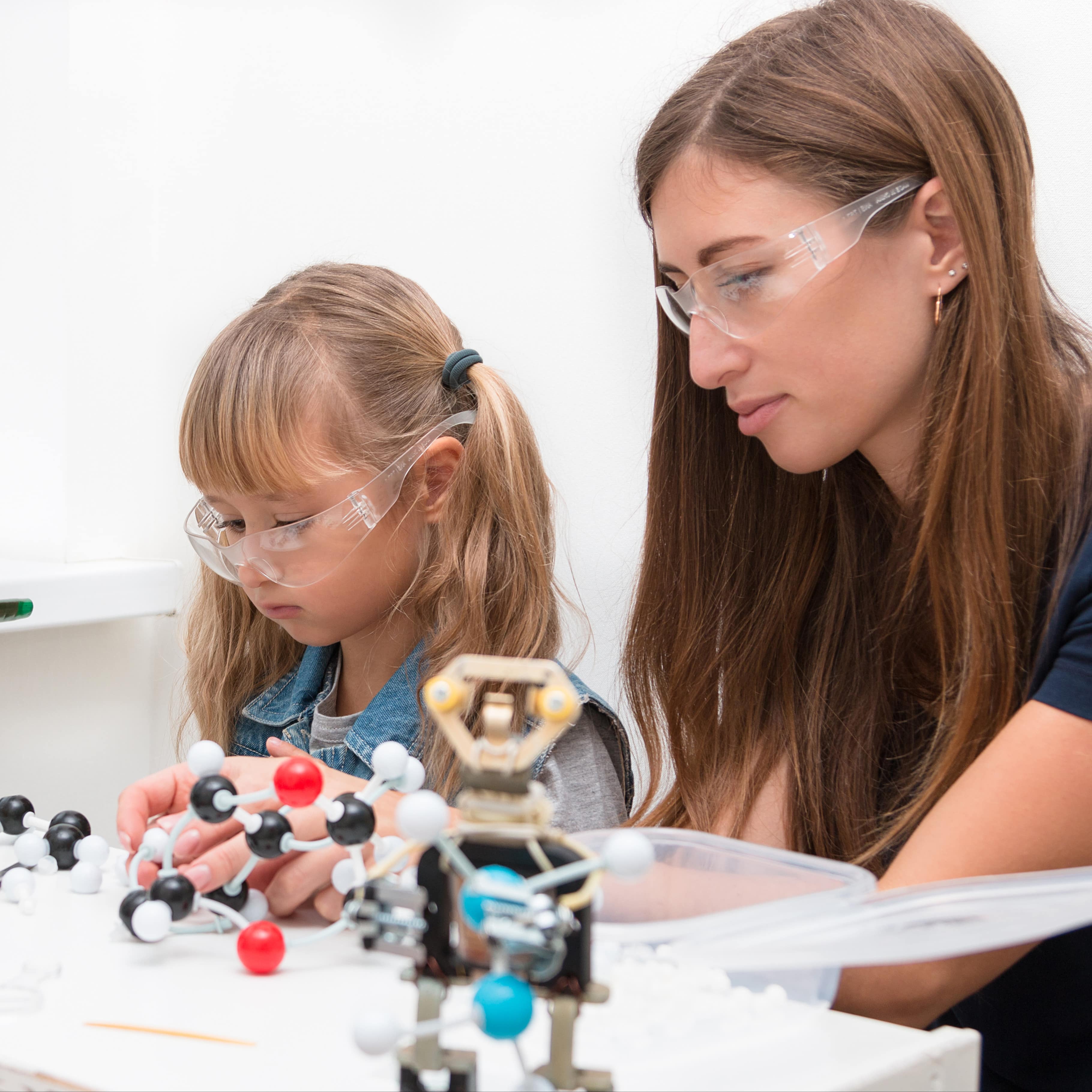 Mutter und Tochter machen ein chemisches Experiment in einem Museum. Beide haben Schutzbrillen auf.