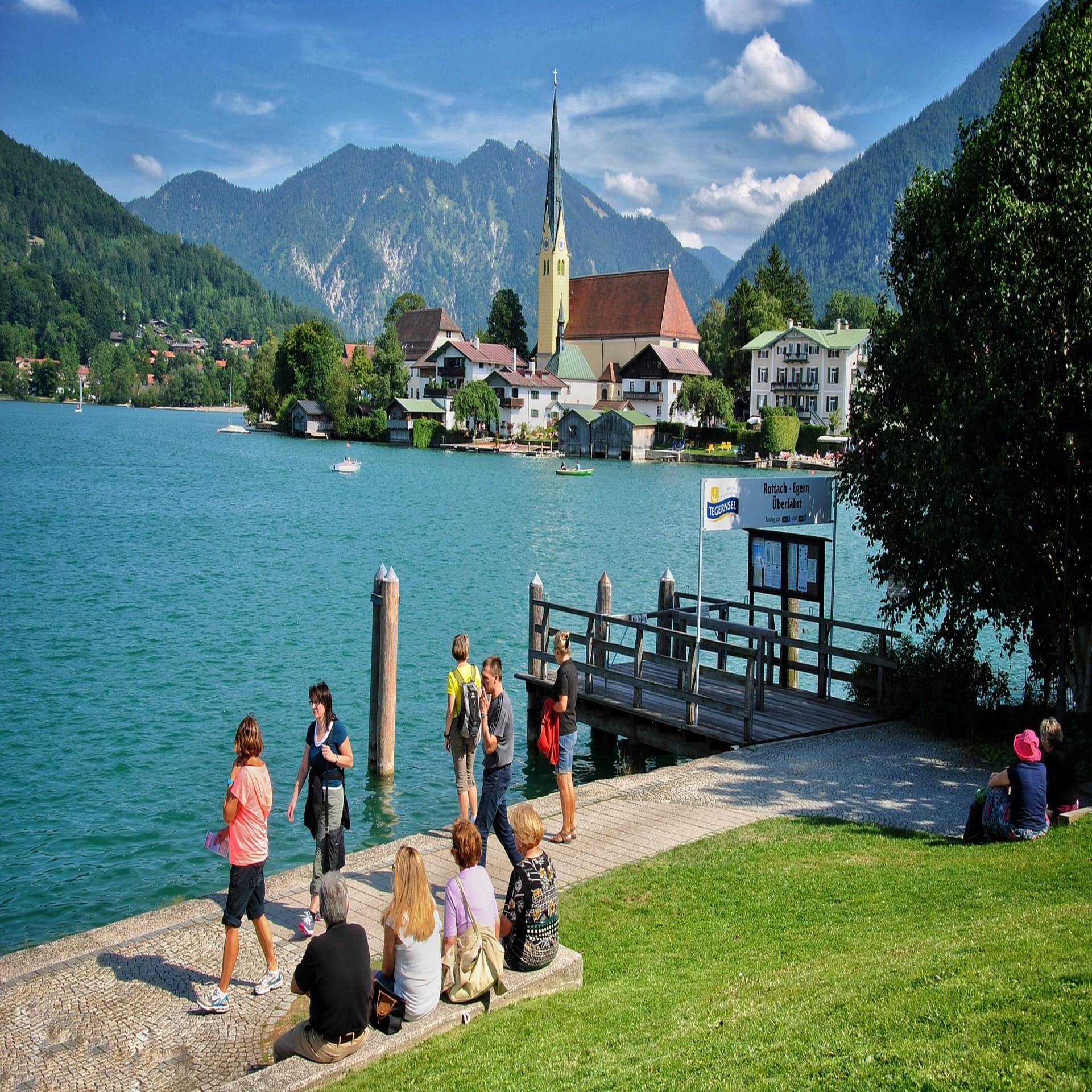 Leute genießen die Sonne an einem Bootsanleger, ein Ort am Tegernsee ist zu sehen