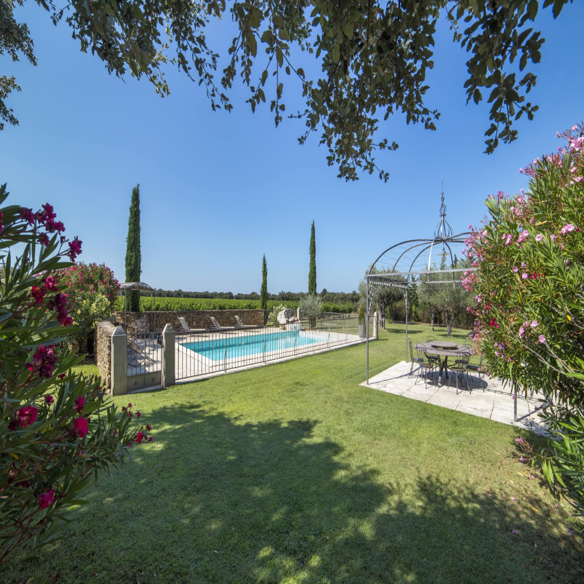 Großes Garten mit eingezäuntem Pool und Blick auf die Weinfelder. Die Sonne scheint.