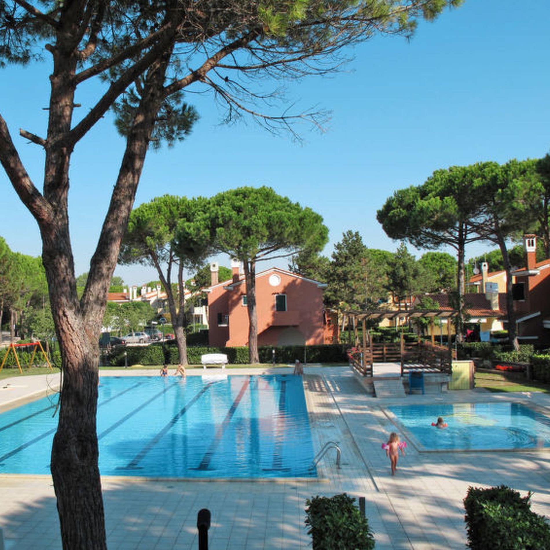 Im Schatten typisch italienischer Kiefern liegen ein großes Schwimmbecken und ein Kinderbecken der Ferienanlage in Bibione