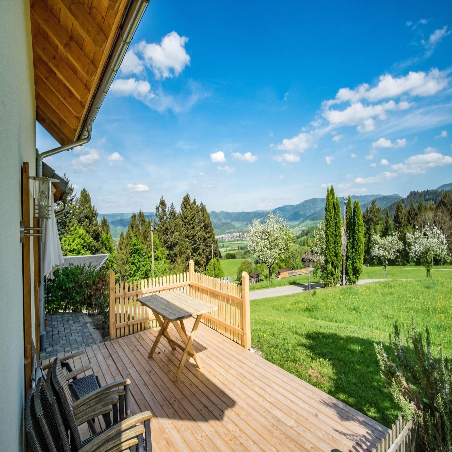 Holzterrasse mit Tisch und Stühlen und Blick auf die umliegende Umgebung bei Sonnenschein.