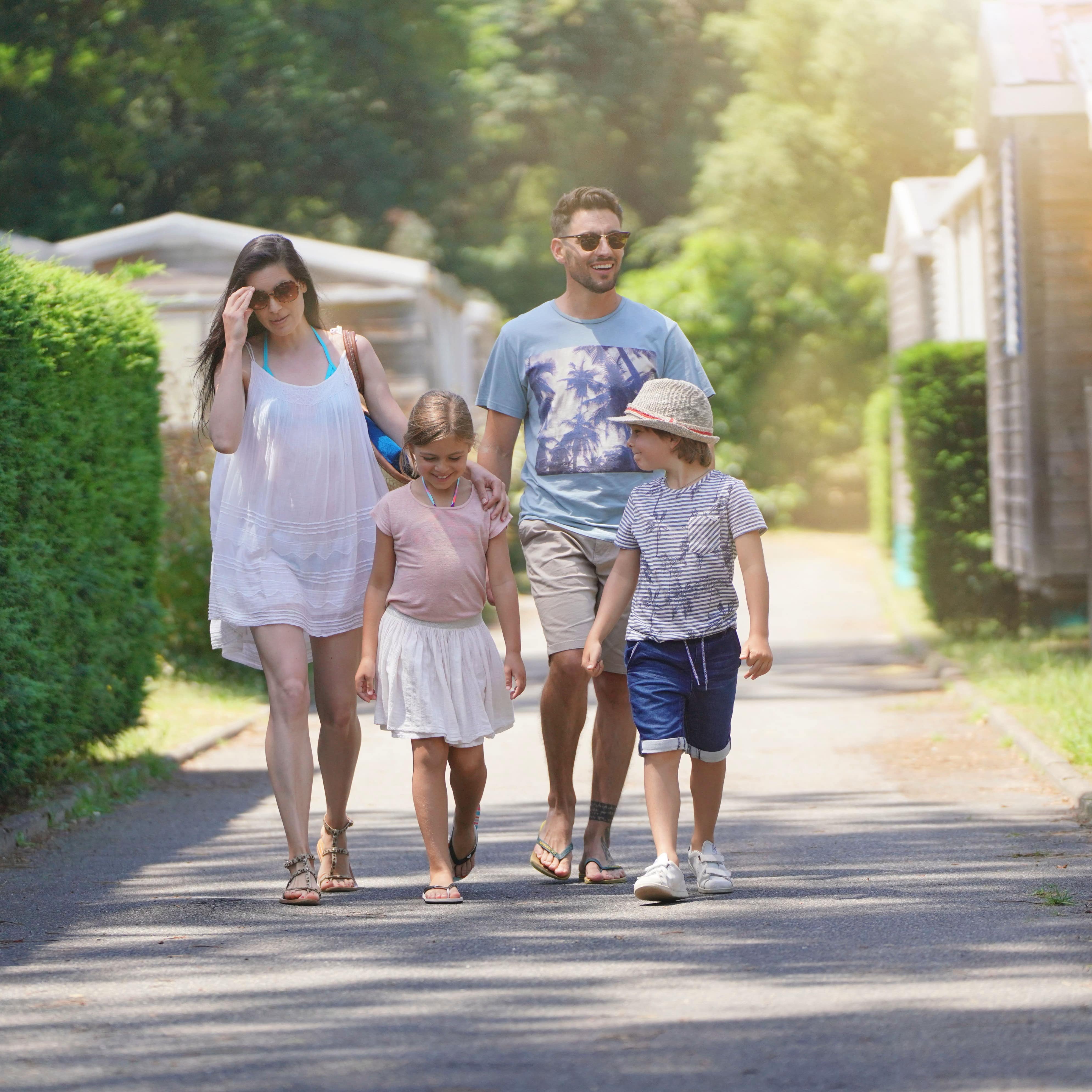 Eltern mit 2 Kindern laufen einen Weg in einem Feriendorf entlang.