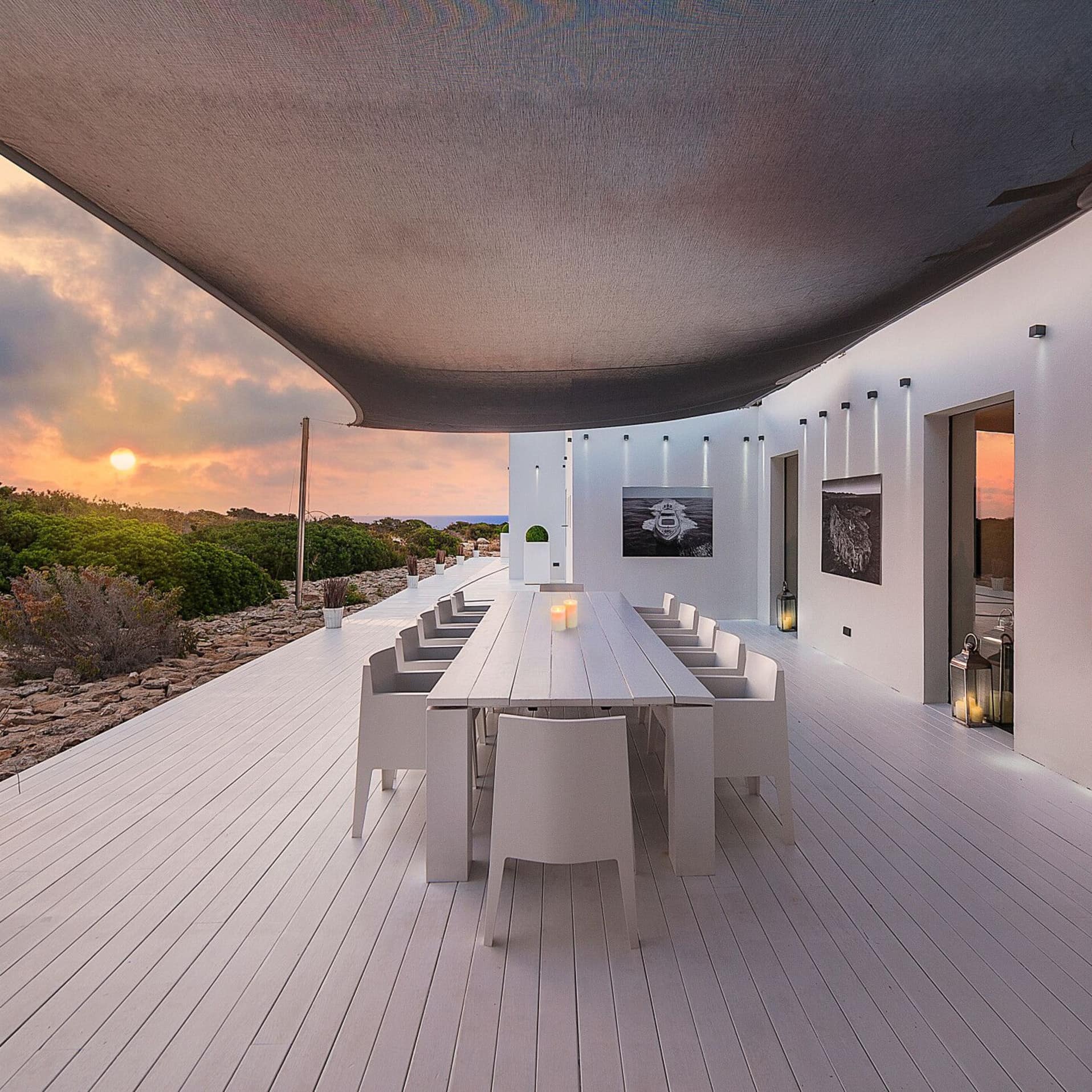 Luxuriöses Ferienhaus beziehungsweise Villa auf Ibiza bei Sonnenuntergang mit weiß getünchter Terrasse, hellen Möbeln und dem Meer im Hintergrund