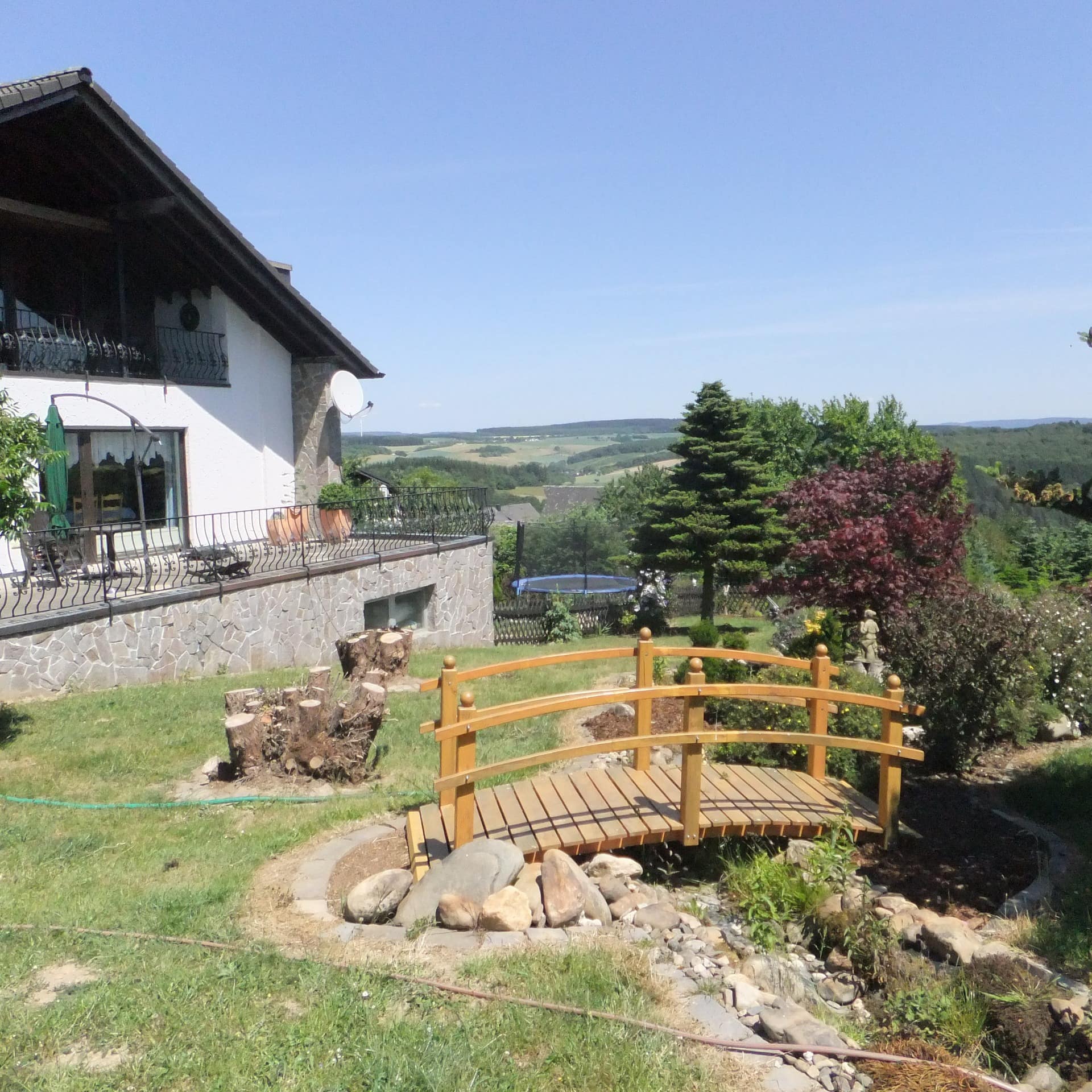 Blick auf den Garten mit kleiner Brücke und Trampolin einer Ferienwohnung im Umland von Trier