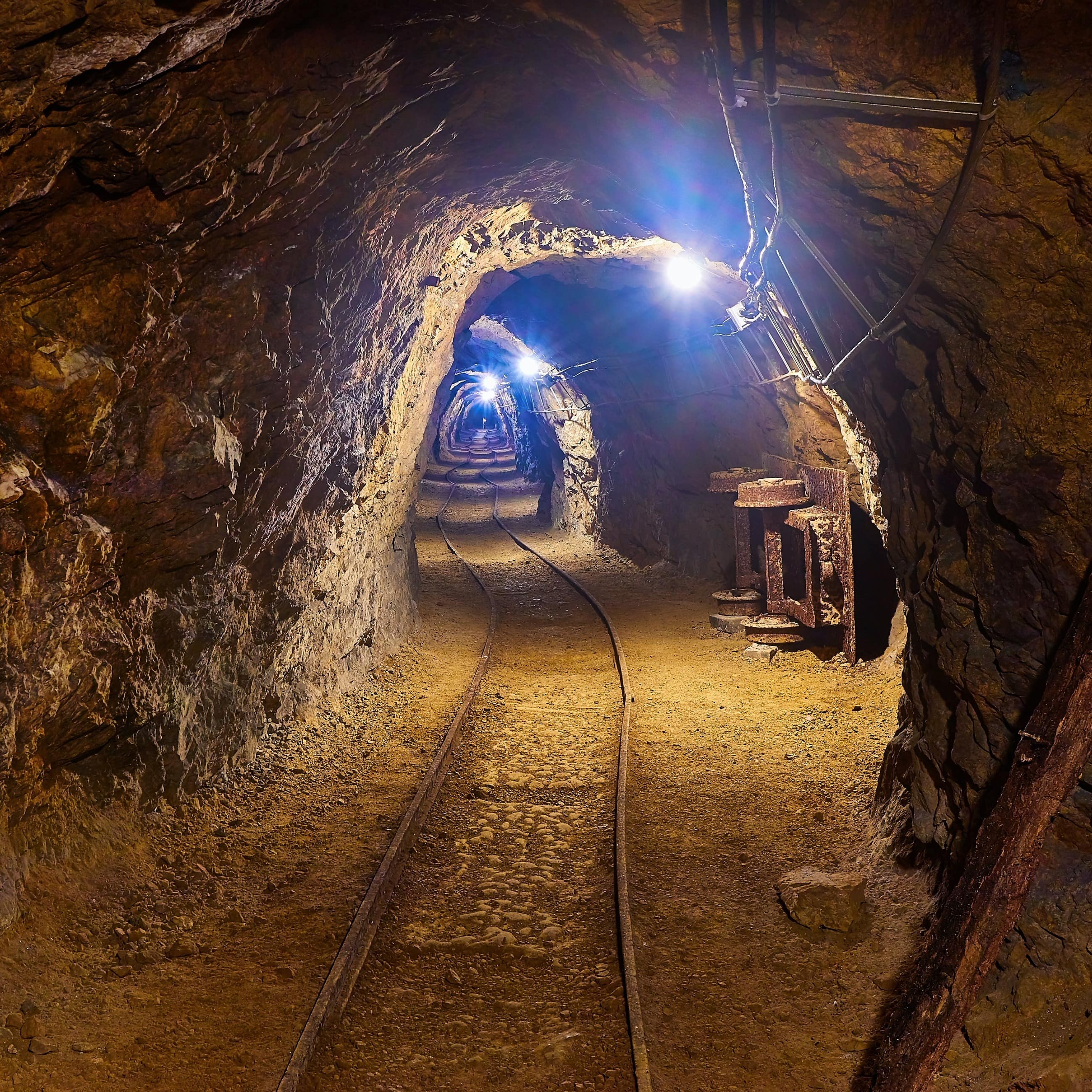 Beleuchteter Tunnel in einem Bergwerk, alte Schienen auf dem Boden.