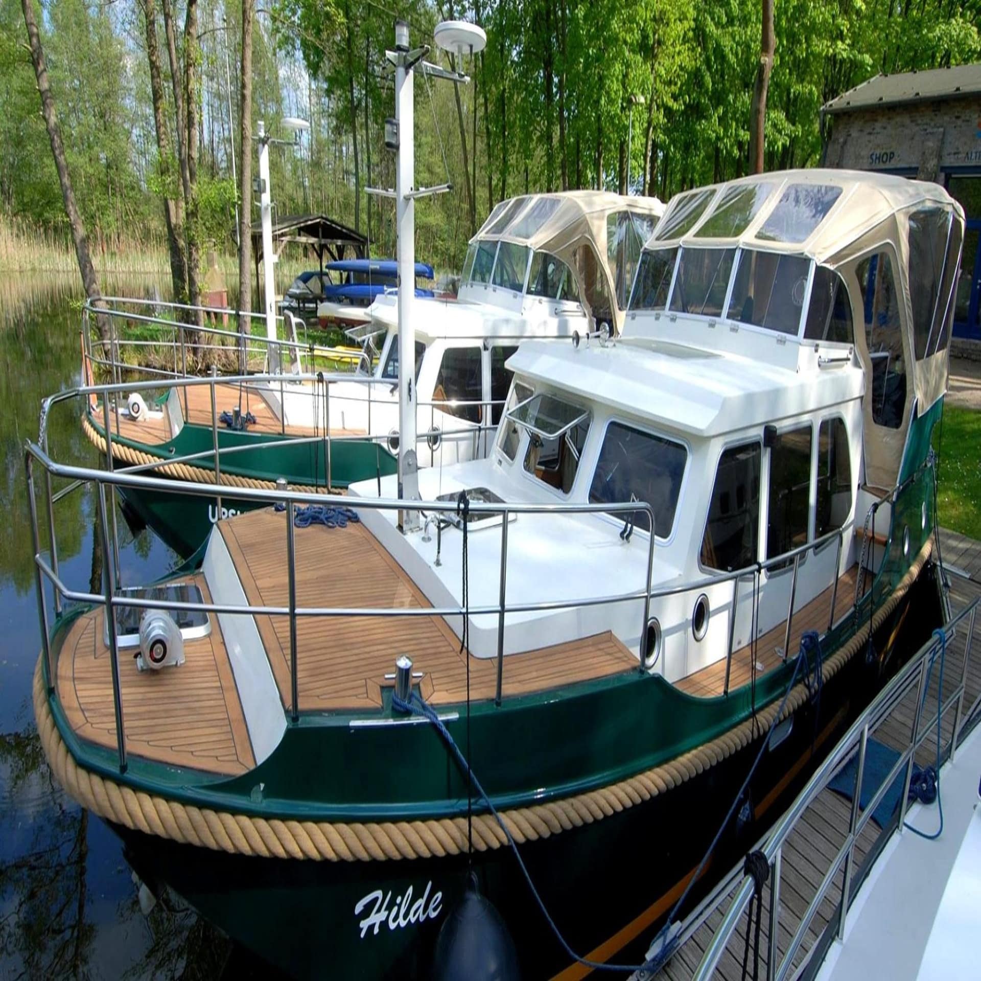 Ein weiß-grünes Boot ankert an einem Anlegeplatz im Wald.
