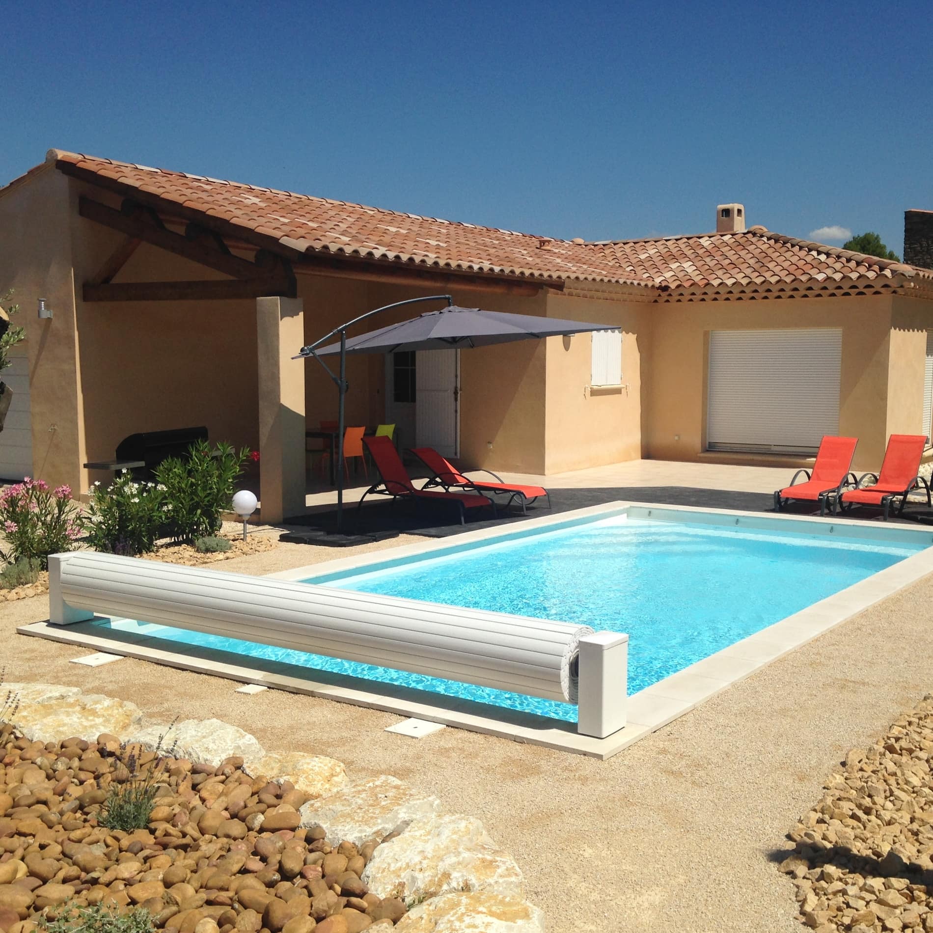Pool mit roten Liegestühlen vor einem einstöckigen, mit runden Ziegeln gedeckten Ferienhaus 