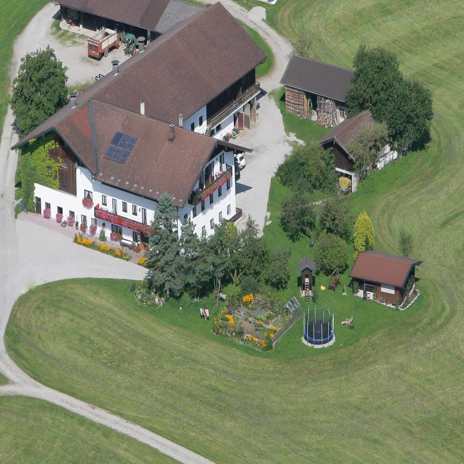 Blick aus der Luft auf einen Gutshof mit Scheune, Traktor und grünem Garten auf einer Wiese. 