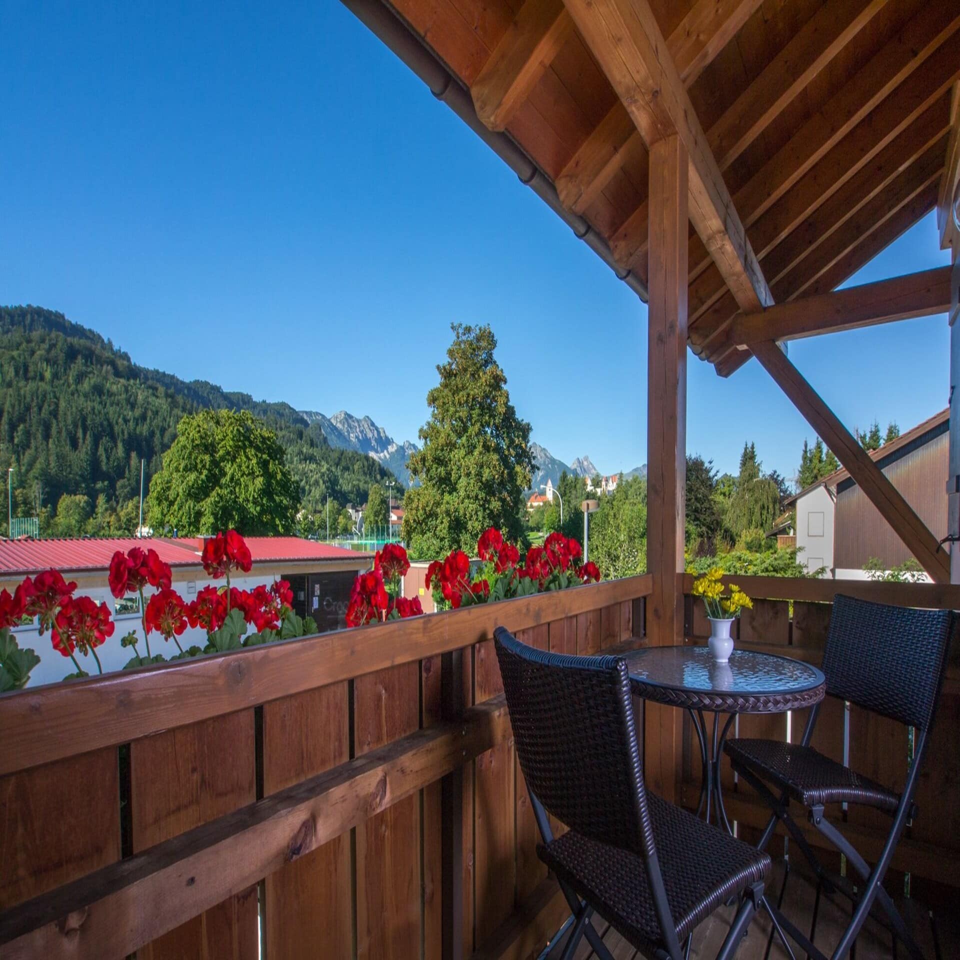 Blick von einem Holzbalkon mit roten Blumen auf das Füssener Umland