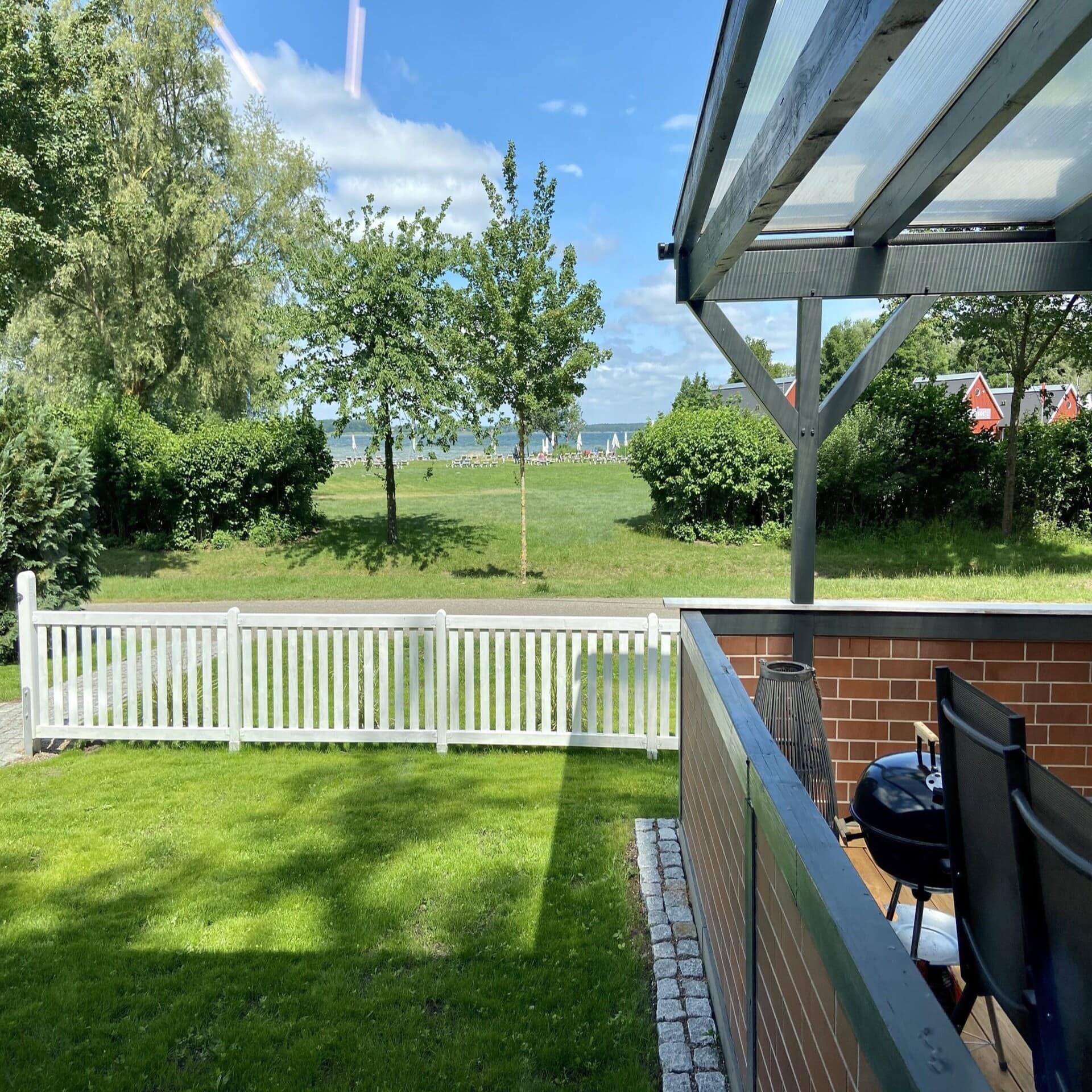 Terrasse und Garten mit Blick über eine Wiese und auf einen See. 