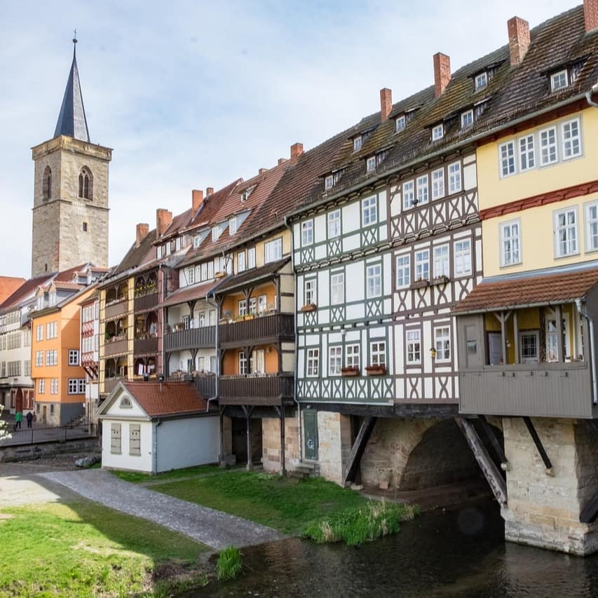Blick auf die Krämerbrücke, die längste bebaute Brücke Europas; auf ihr stehen Fachwerkhäuser, im Hintergrund ist ein Kirchturm zu sehen.