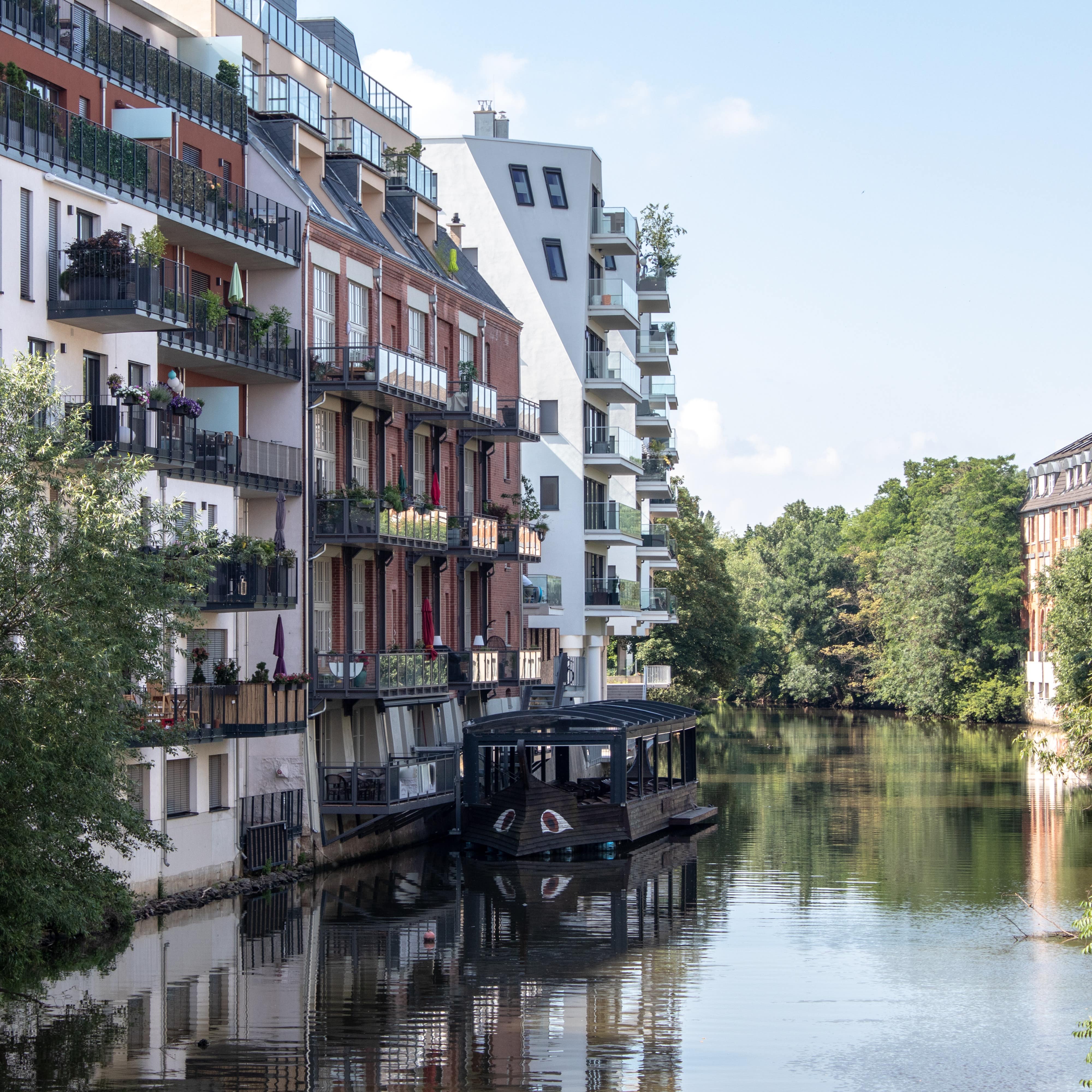 Blick über den Fluss auf Apartmenthäuser direkt am Wasser, davor ankert ein Boot.