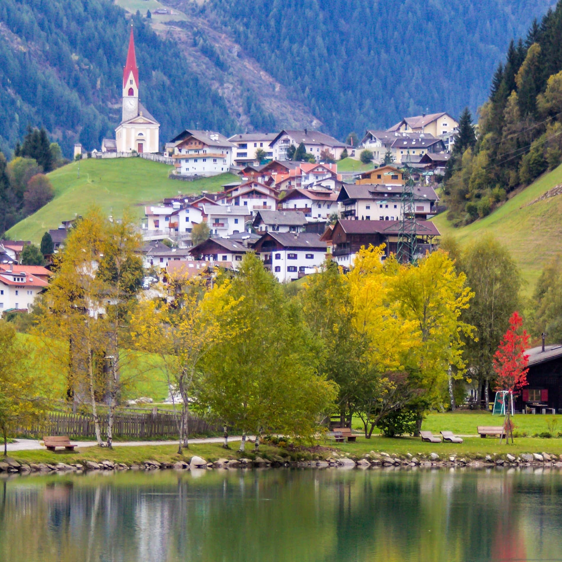 Südtiroler Dorf in den Dolomiten an einem See mit Gebäuden, die teilweise als Ferienhäuser gemietet werden können