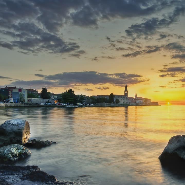 Blick auf die Promenade und Häuser von Poreč direkt am Wasser bei Sonnenuntergang. 