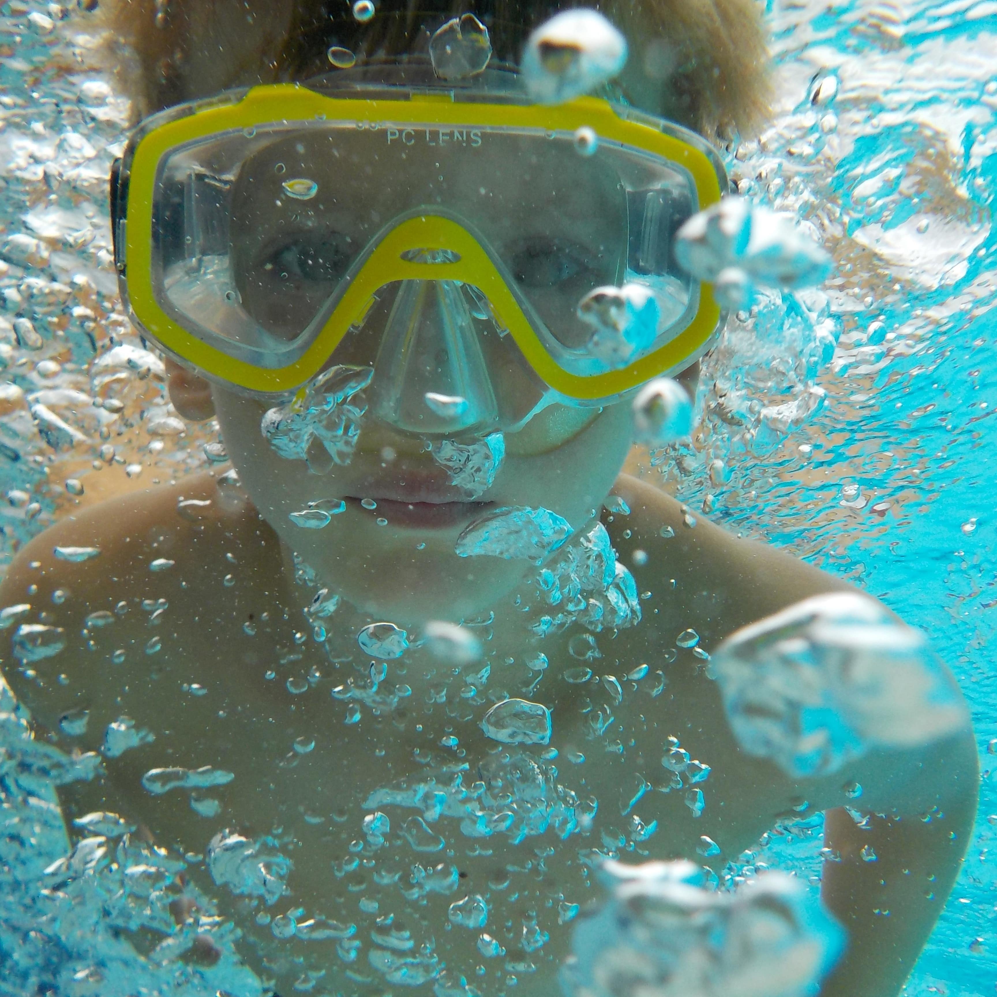 Nahaufnahme: Junge mit Taucherbrille Unterwasser, umgeben von Luftblasen.