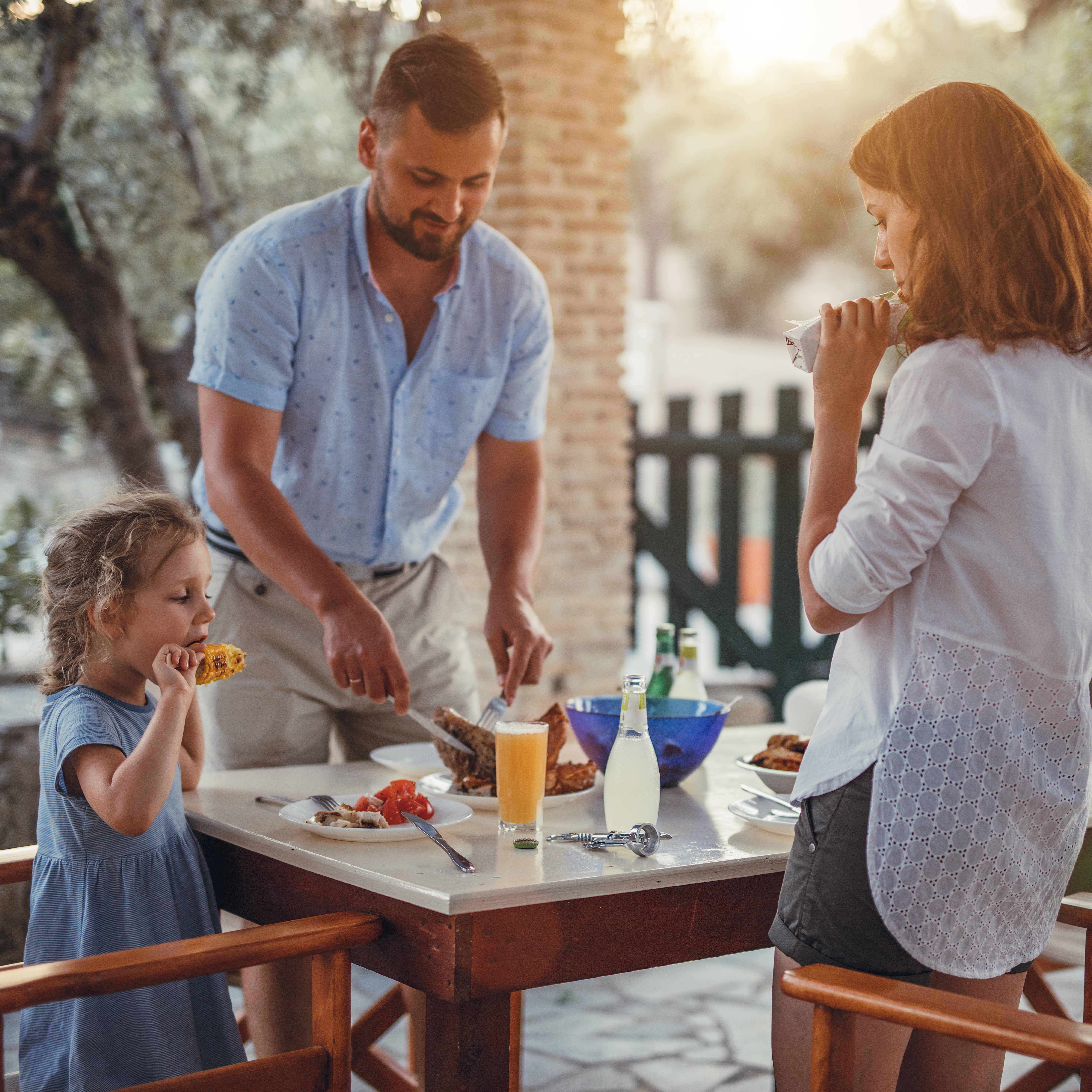 Eltern und Tochter am Tisch auf einer Terrasse, es gibt mediterranes Essen.