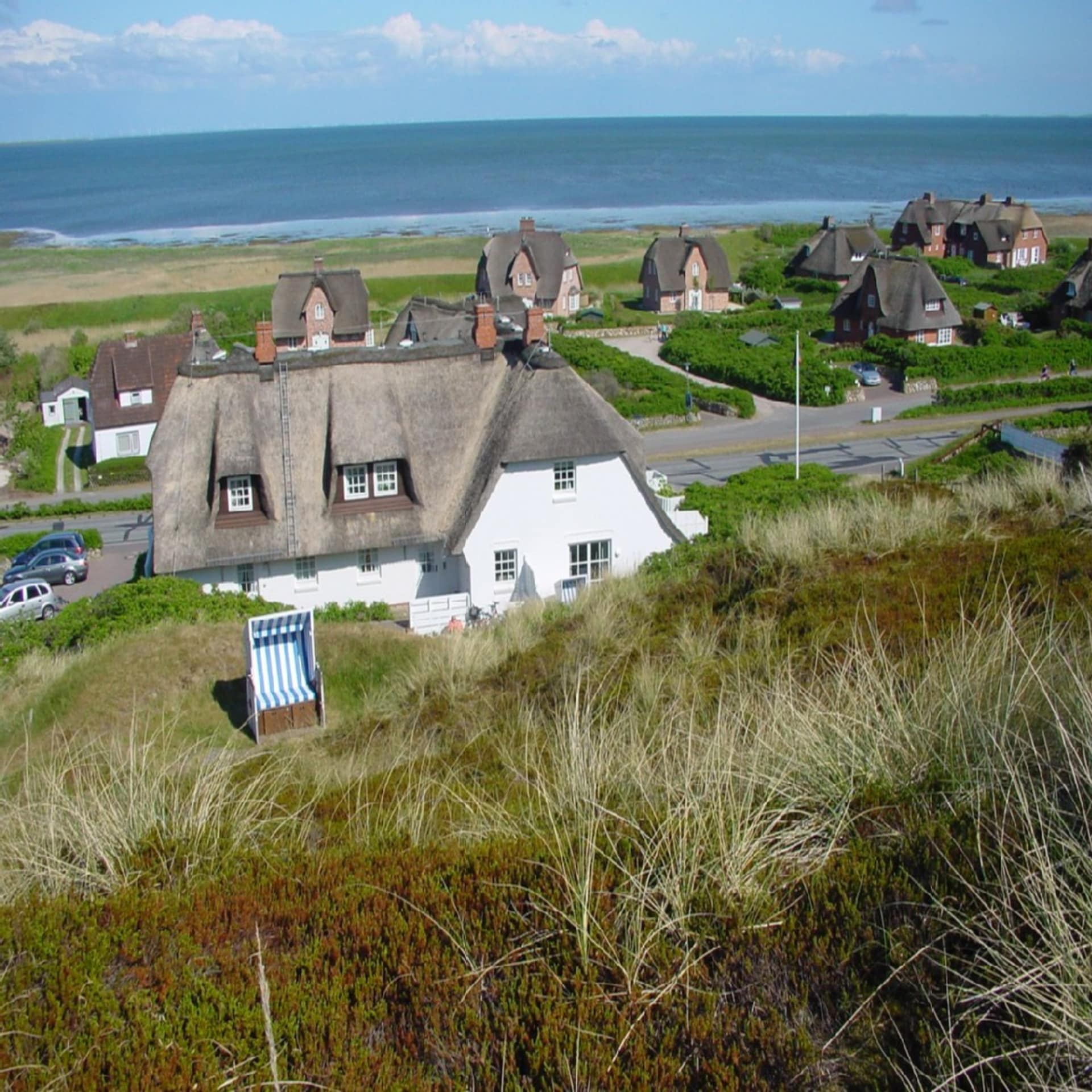  Blick von einem Hügel auf Reetdachhäuser am Strand von Sylt.