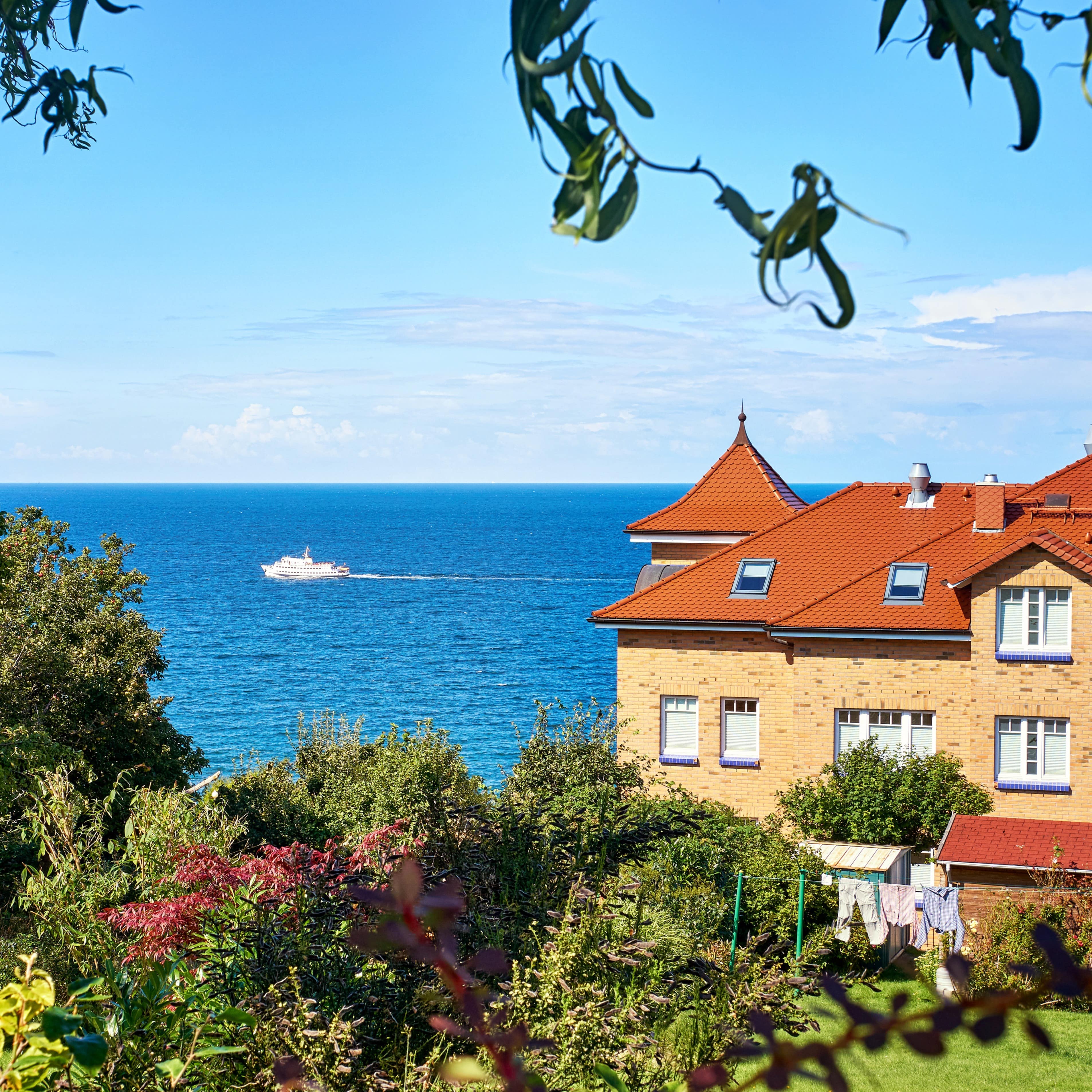 Blick in einen Garten und auf ein Haus auf Rügen, zwischen Bäumen und Haus sieht man das Meer.